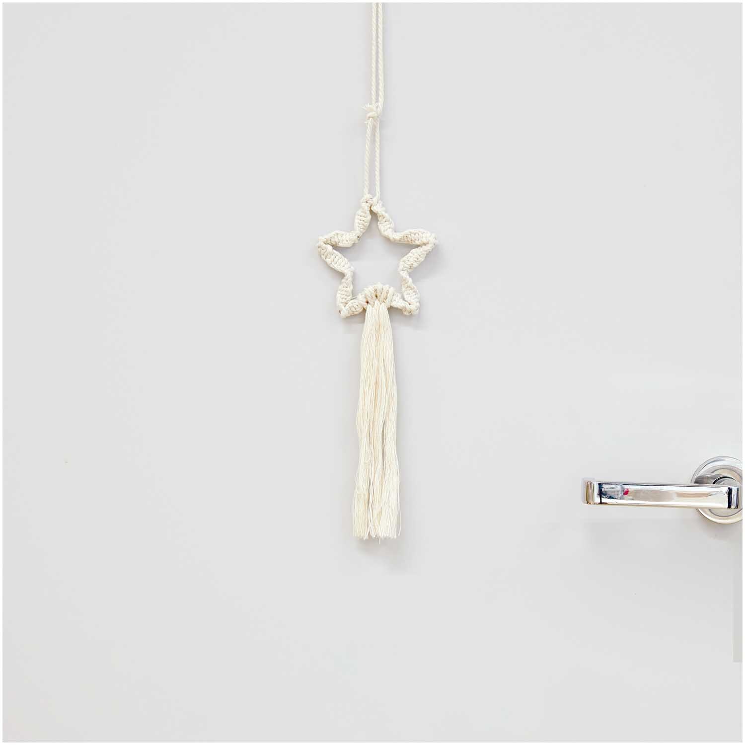 Set macramé étoile 25x11cm from Rico Design Makramee Set Stern 25x11cm von Rico Design: Ein cremefarbener Makramee-Stern hängt an einer Tür.