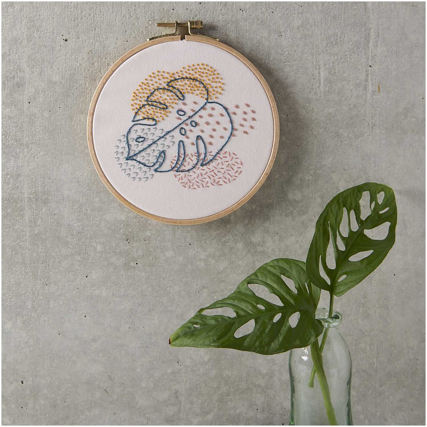 Pack de broderie Slow Evenings Monstera image Ø 15,5cm from Rico Design Stickpackung Slow Evenings Monstera Bild Ø 15,5cm zeigt ein gesticktes Monstera-Motiv in bunten Farben an einer grauen Wand.