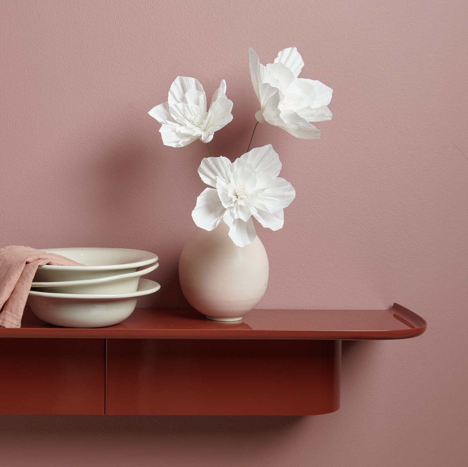 Krepppapier Blüten in einer Vase auf einem Regal, umgeben von Geschirr, dekorieren den Raum stilvoll.