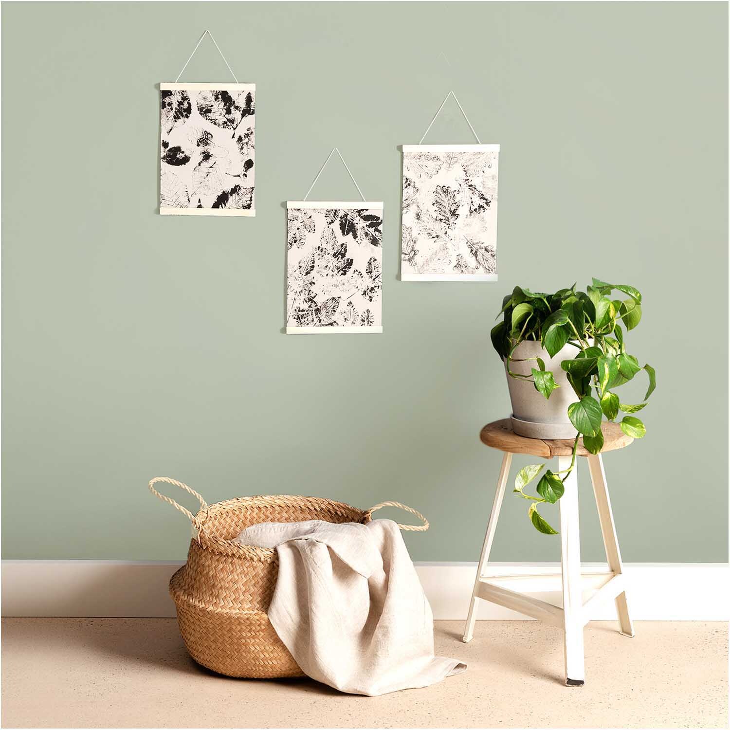Porte-affiche en bois 20cm from Rico Design Posterhänger Holz 20cm: Drei Poster mit abstrakten Mustern an einer grünen Wand, neben einem Korb und einer Pflanze.