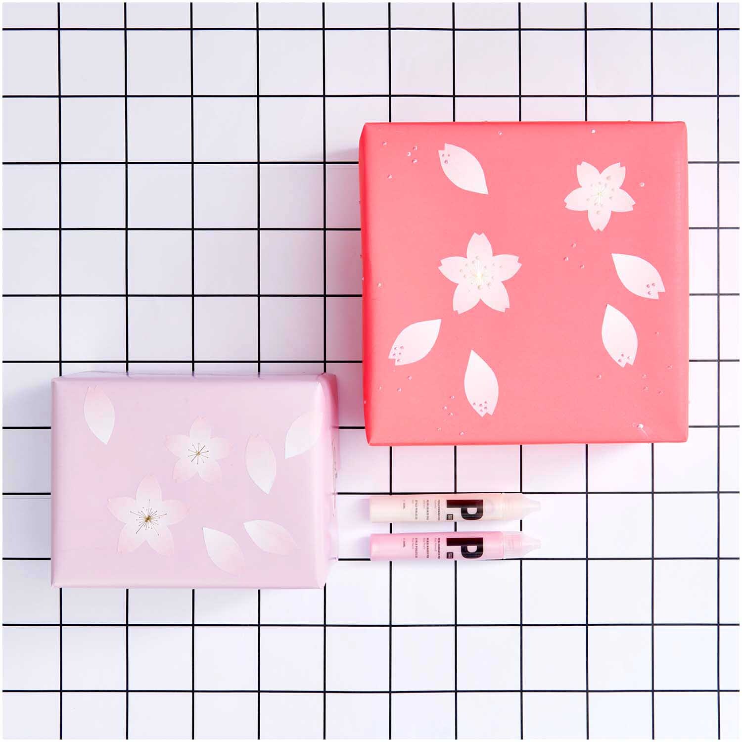 Paper Poetry Sticker Blütenblätter auf Geschenkboxen in Rosa und Pink, dekoriert auf kariertem Hintergrund. Ideal für kreative Verpackungen.