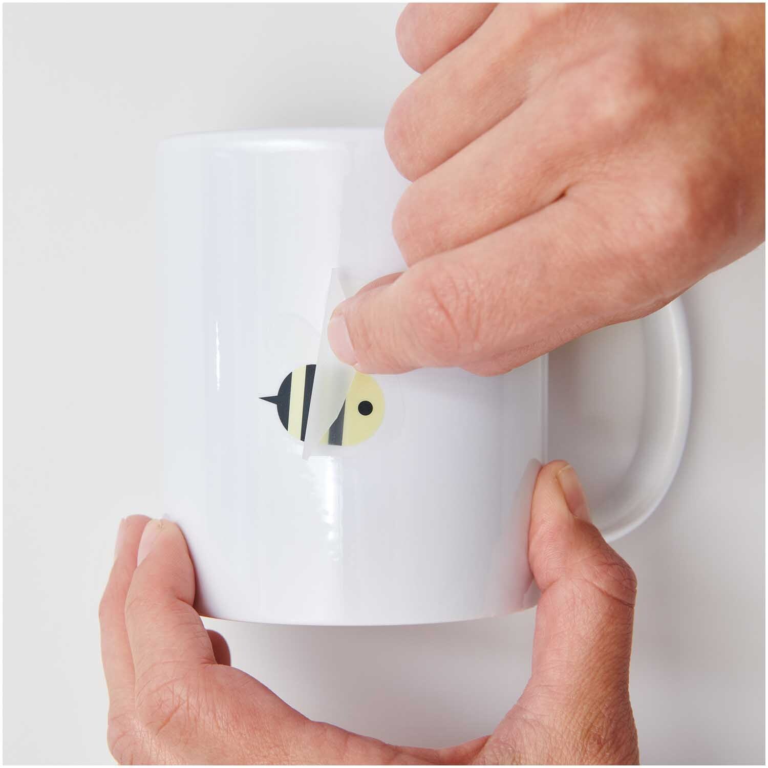 Transfermotiv Biene 15 Stück von Rico Design Transfermotiv Biene: Hände kleben ein Bienenmotiv von Rico Design auf eine weiße Tasse.