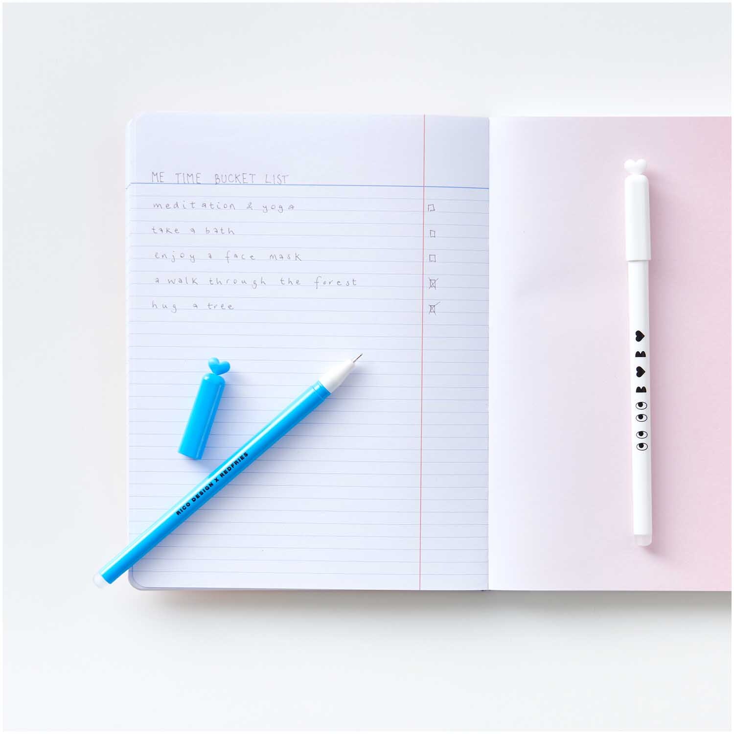 Rico Design x Redfries Gelstifte schwarz 0,4mm 2 Stück von Rico Design Rico Design x Redfries Gelstifte, 0,4mm, 2 Stück, neben einem offenen Notizbuch auf einem Tisch.