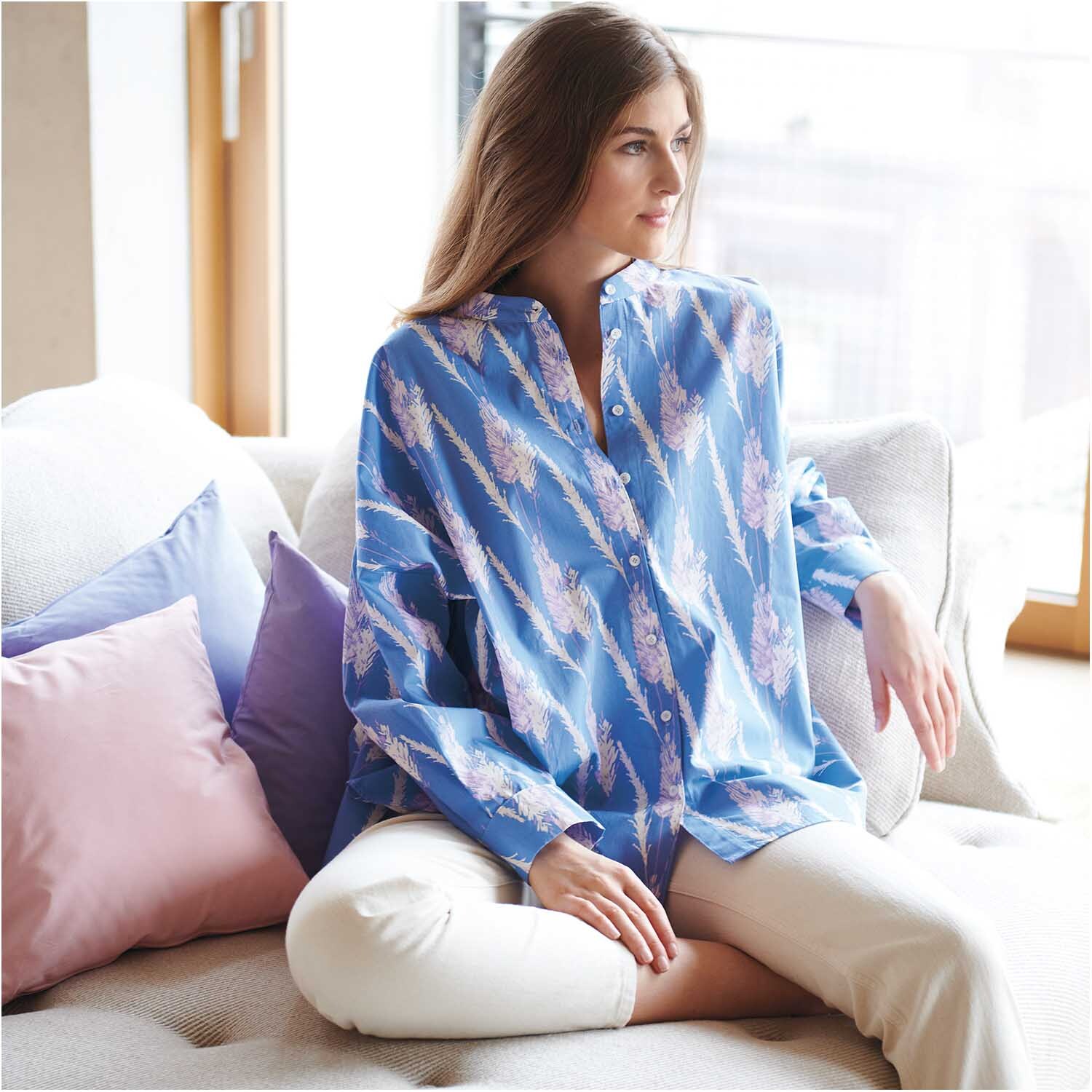 Stoffabschnitt Druckstoff Pampasgras azur 50x140cm von Rico Design Stoffabschnitt Druckstoff Pampasgras azur zeigt eine Frau in blauer Bluse auf einem Sofa sitzend.