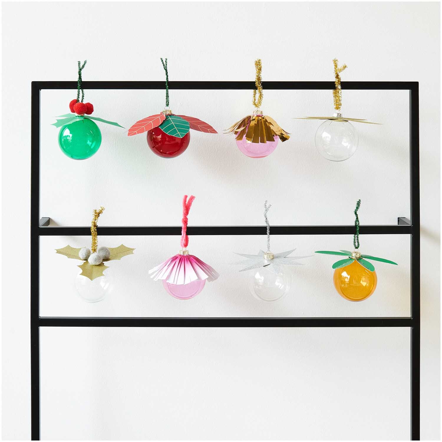 Paper Poetry Christbaumkugel-Topper Stern silber 6 Stück von Rico Design Paper Poetry Christbaumkugel-Topper Stern silber 6 Stück von Rico Design. Bunte Christbaumkugeln in verschiedenen Designs hängen an einem schwarzen Gestell.