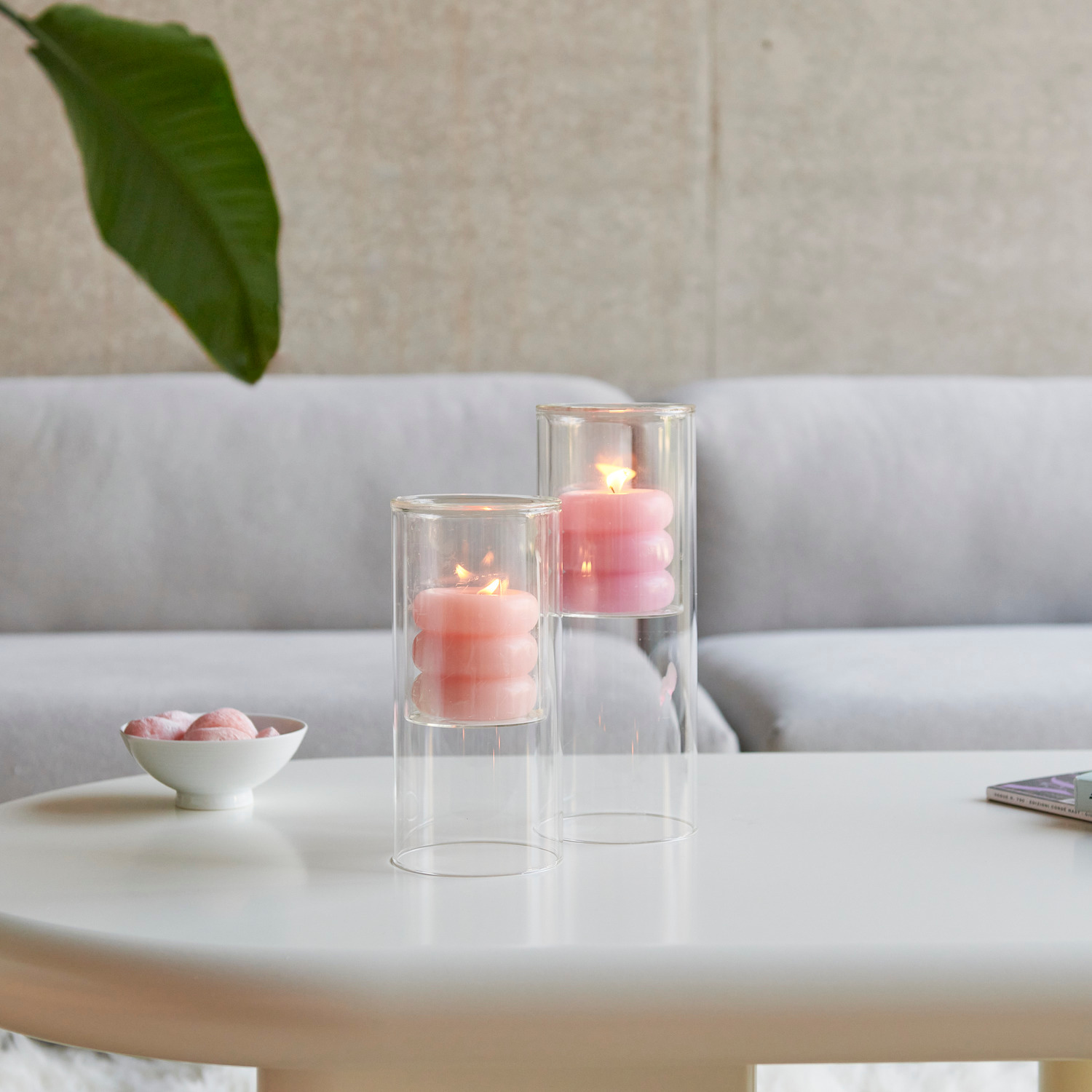 Glas-Windlicht mit Stumpenkerze in stilvoller Glasvase auf einem Tisch, umgeben von moderner Einrichtung.