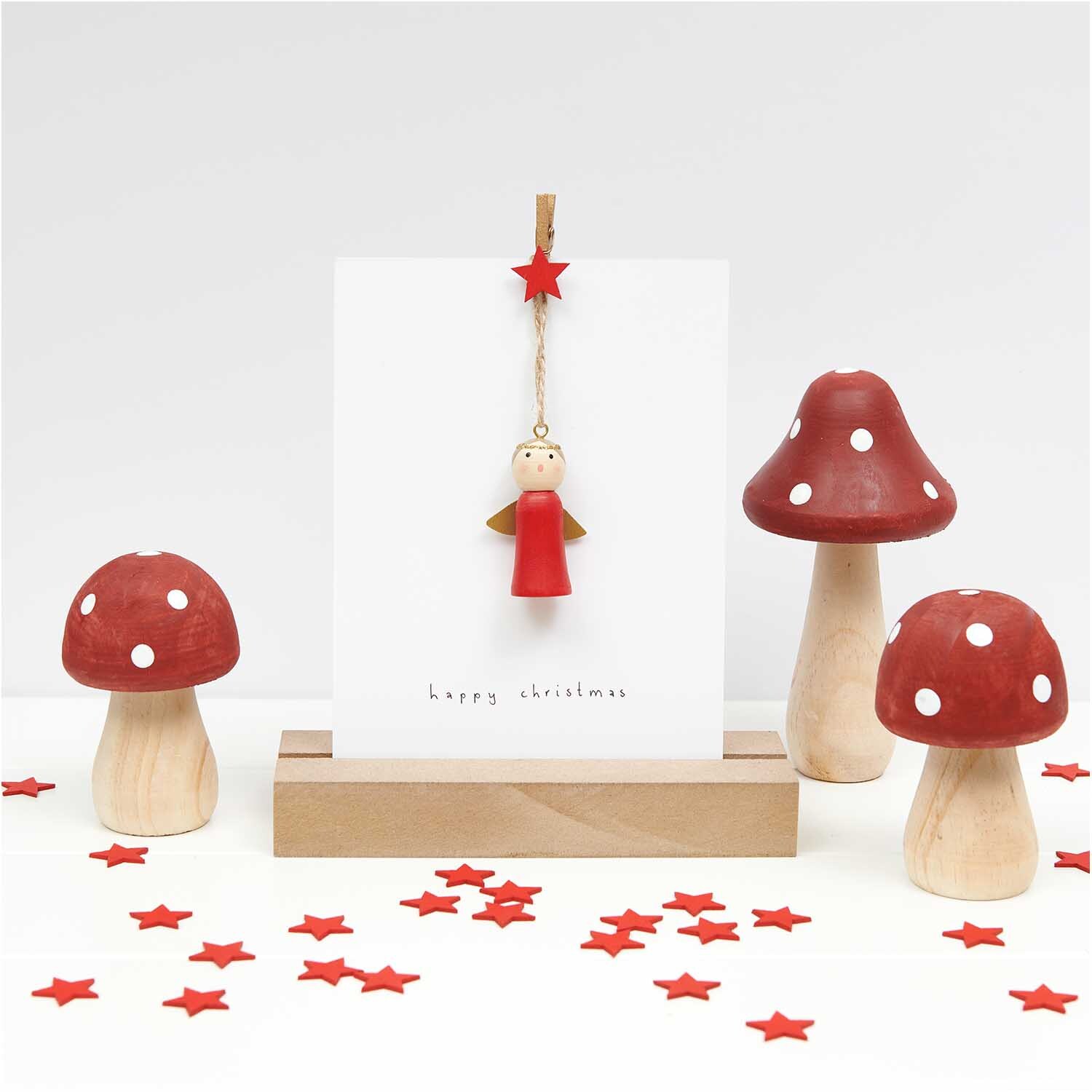 Dekoklammern Stern rot 3cm 8 Stück von Rico Design Dekoklammern Stern rot 3cm 8 Stück von Rico Design: Rote Sternklammer hält Karte mit Engel, umgeben von roten Pilzen und Sternen auf weißem Hintergrund.