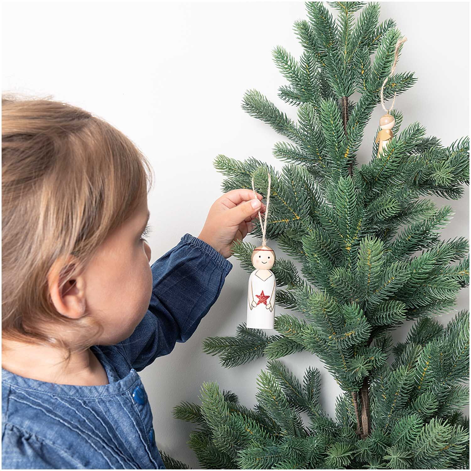 Holzhänger Engel mit Stern wird von einem Kind an einen grünen Tannenbaum gehängt. Marke: Rico Design.