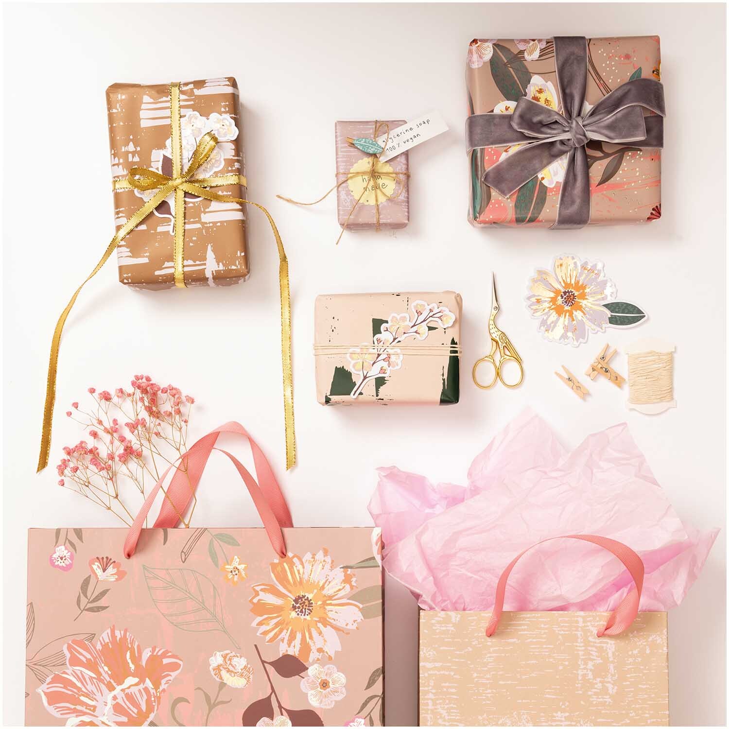 Paper Poetry Geschenkpapier Natur Blumen mauve, dekorativ verpackte Geschenke mit rosa und goldenen Akzenten, umgeben von Bastelmaterialien.