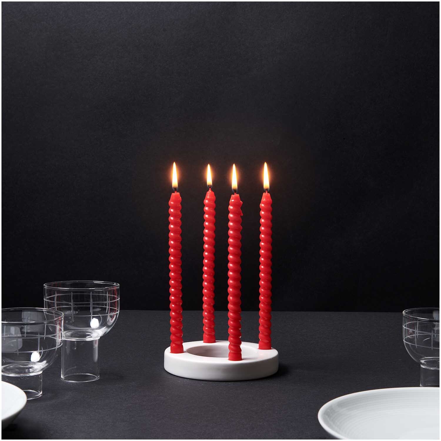 Adventskranz Keramik weiß 12,5cm mit vier brennenden roten Kerzen, umgeben von Gläsern und Tellern auf schwarzem Hintergrund.