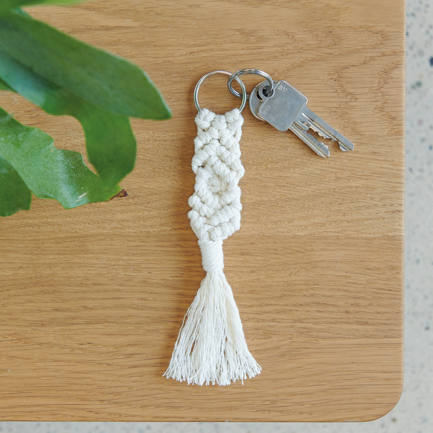 Set de macramé porte-clés 3 pièces from Rico Design Makramee Set Schlüsselanhänger, 3 Stück, aus cremefarbenem Garn auf Holztisch mit Schlüsselring.