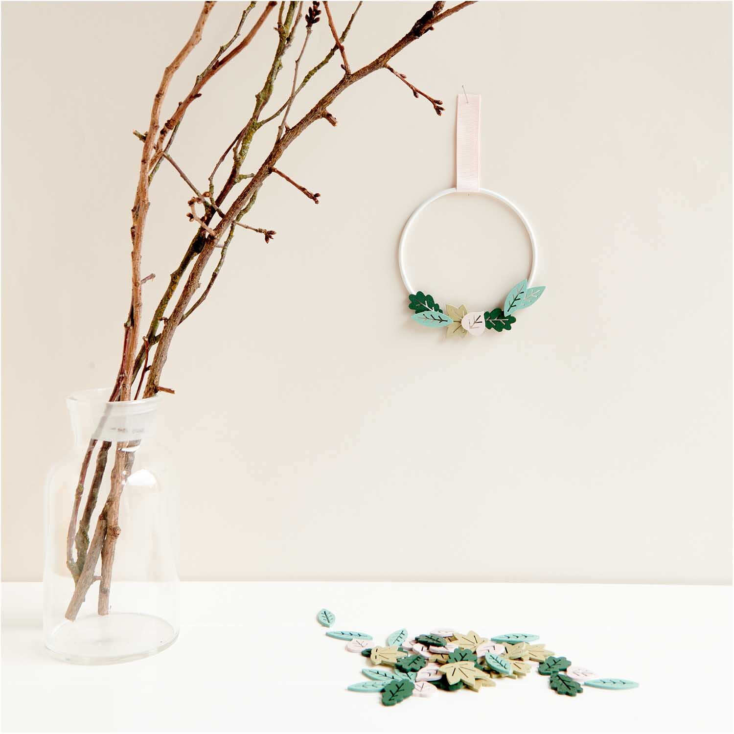 Wood litter leaves mix green 48 pieces from Rico Design Holzstreu Blätter Mix grün 48 Stück, dekorativ arrangiert auf weißem Tisch neben Vase mit Zweigen.