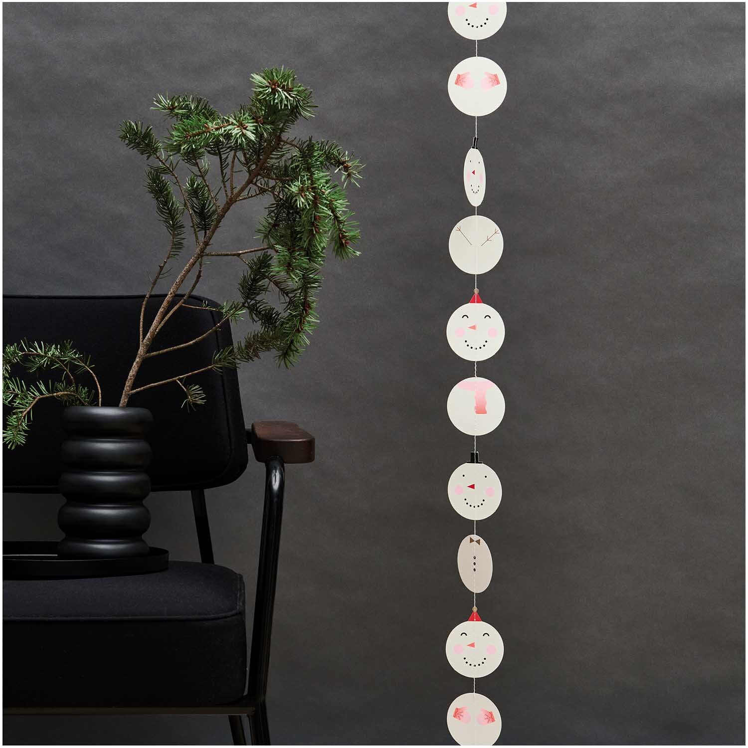 Paper Poetry Genähte Girlande Schneemänner 2,3m von Rico Design Paper Poetry Genähte Girlande Schneemänner 2,3m: Weiße Schneemann-Girlande von Rico Design, dekorativ an schwarzem Stuhl und Pflanze.