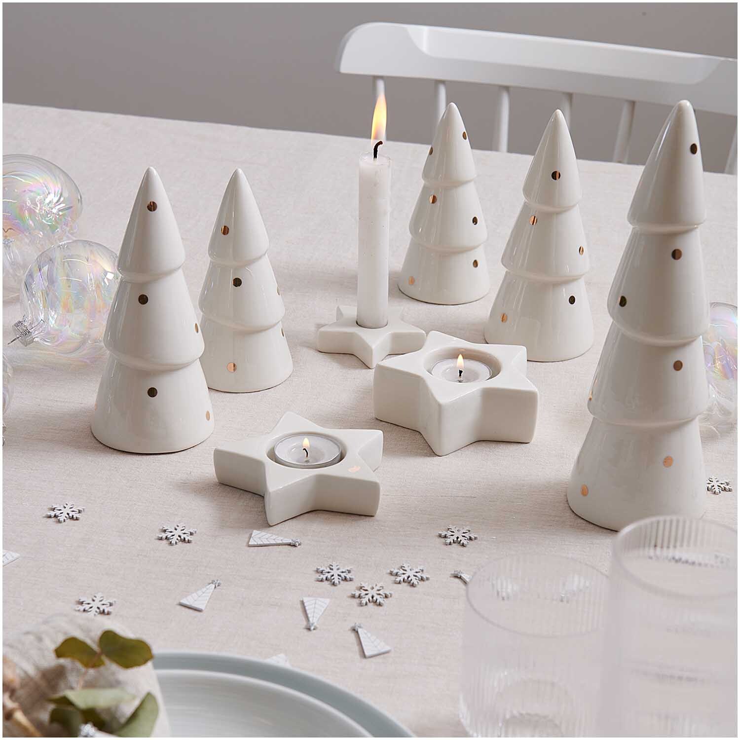 Tannenbaum aus Porzellan weiß-gold-gepunktet Größe 8,2x25cm von Rico Design Tannenbaum aus Porzellan weiß-gold-gepunktet, dekorativ auf Tisch arrangiert, umgeben von Kerzen und Sternen. Ideal für festliche Dekoration.