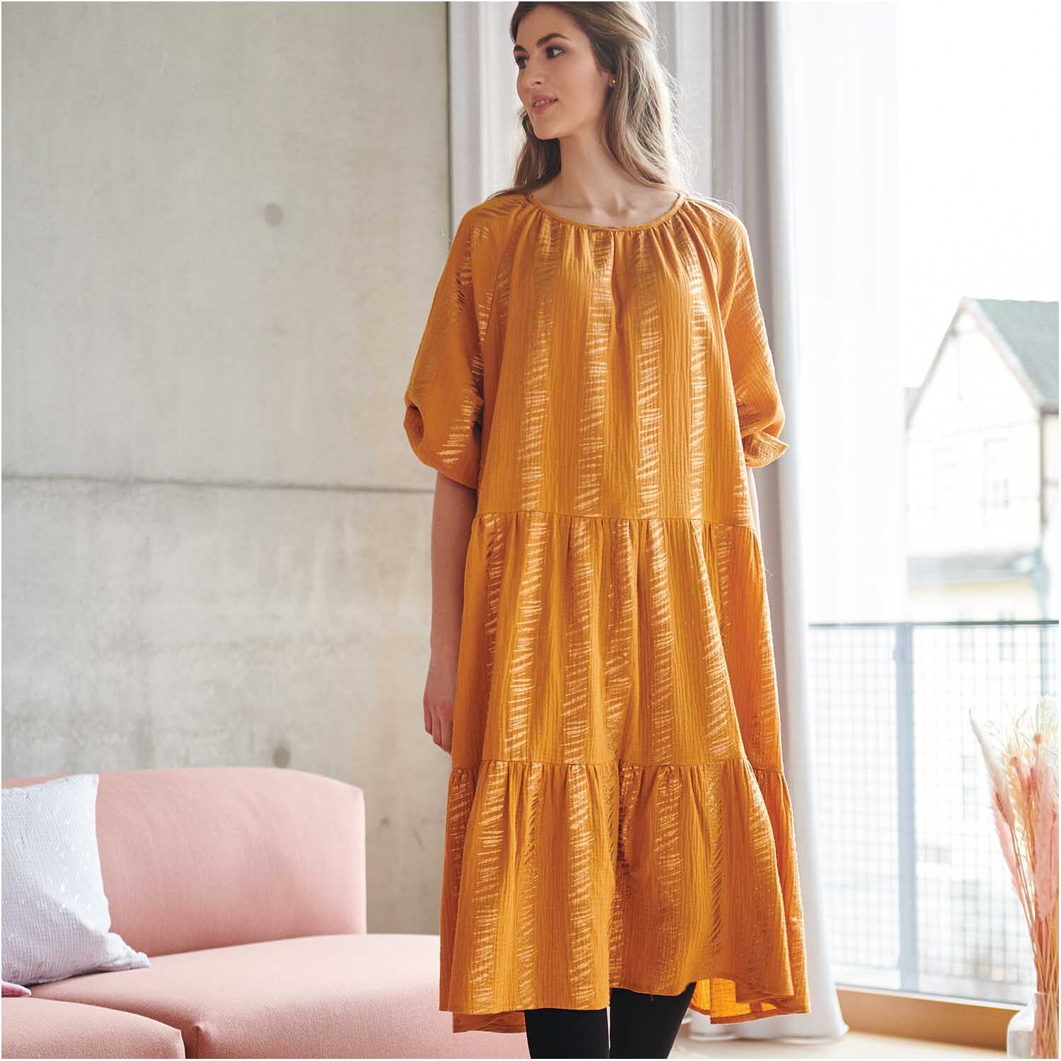 Meterware Krinkelmusselin senf Hot Foil von Rico Design Meterware Krinkelmusselin senf Hot Foil: Frau in senffarbenem Kleid von Rico Design in modernem Wohnzimmer.