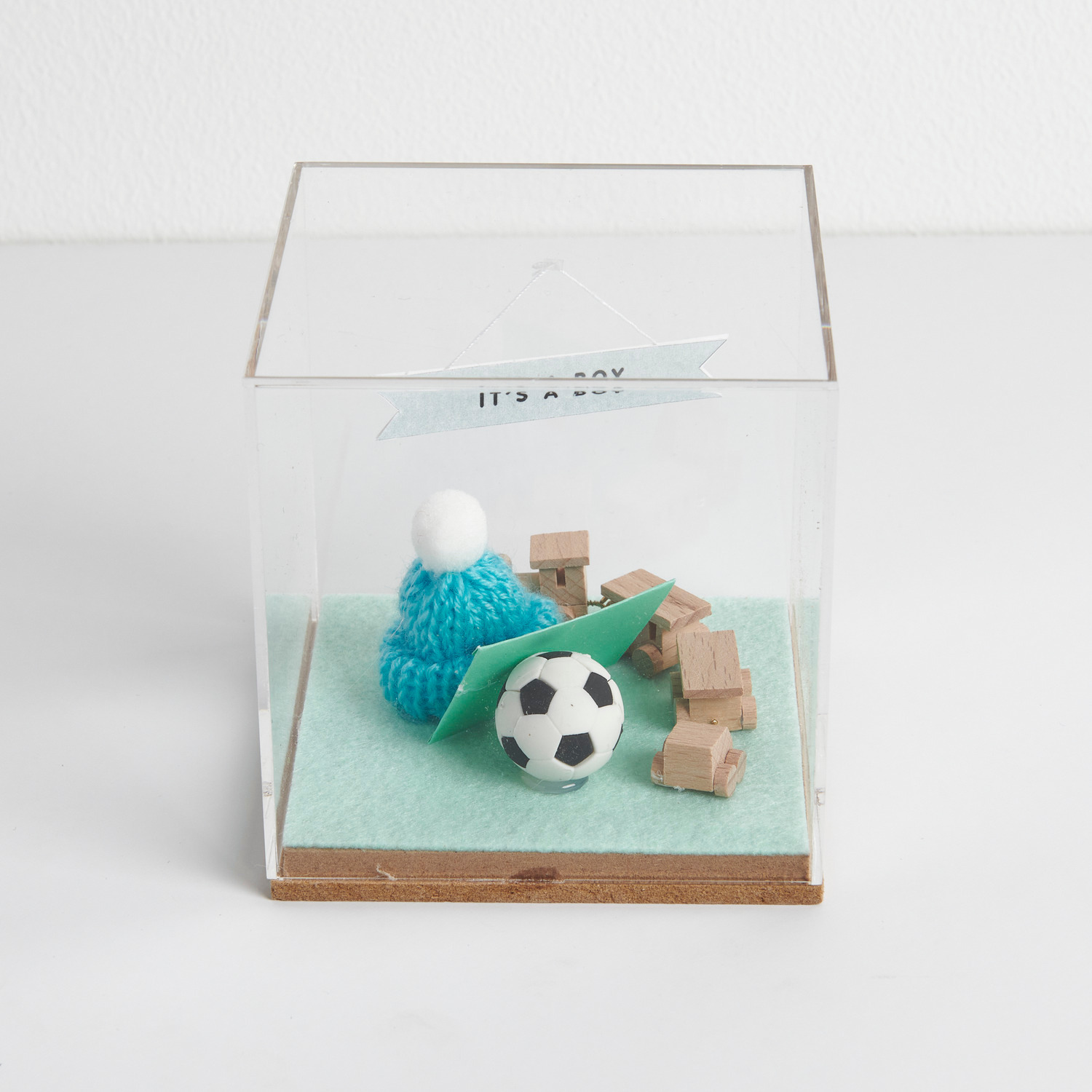 Figurico Dekohaube Würfel Größe 6x6x6,5cm von Rico Design Figurico Dekohaube Würfel mit Miniatur Fußball, blauem Strickmütze und Holzwürfeln in einer transparenten Box.