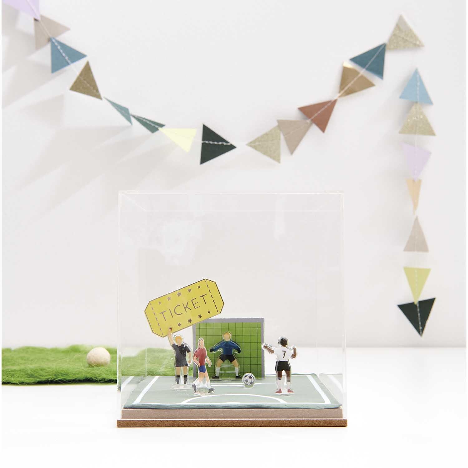 Figurico Gelsticker Fußballspieler von Rico Design Figurico Gelsticker Fußballspieler: Miniatur-Fußballszene in Vitrine, dekoriert mit bunten Wimpeln.