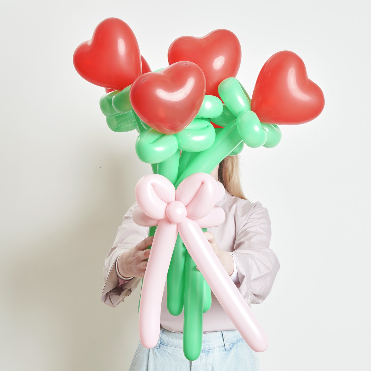 Ballonstrauß Herzen Rot 60cm 14 Stück von Rico Design Ballonstrauß Herzen Rot: Frau hält Strauß aus roten Herzballons mit grünen Stielen und rosa Schleife.
