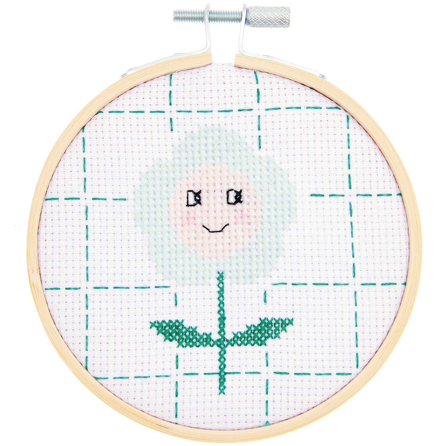 Stickpackung Happy Flower: Ein Stickrahmen mit einem lächelnden Blumenmotiv auf weißem Stoff von Rico Design.