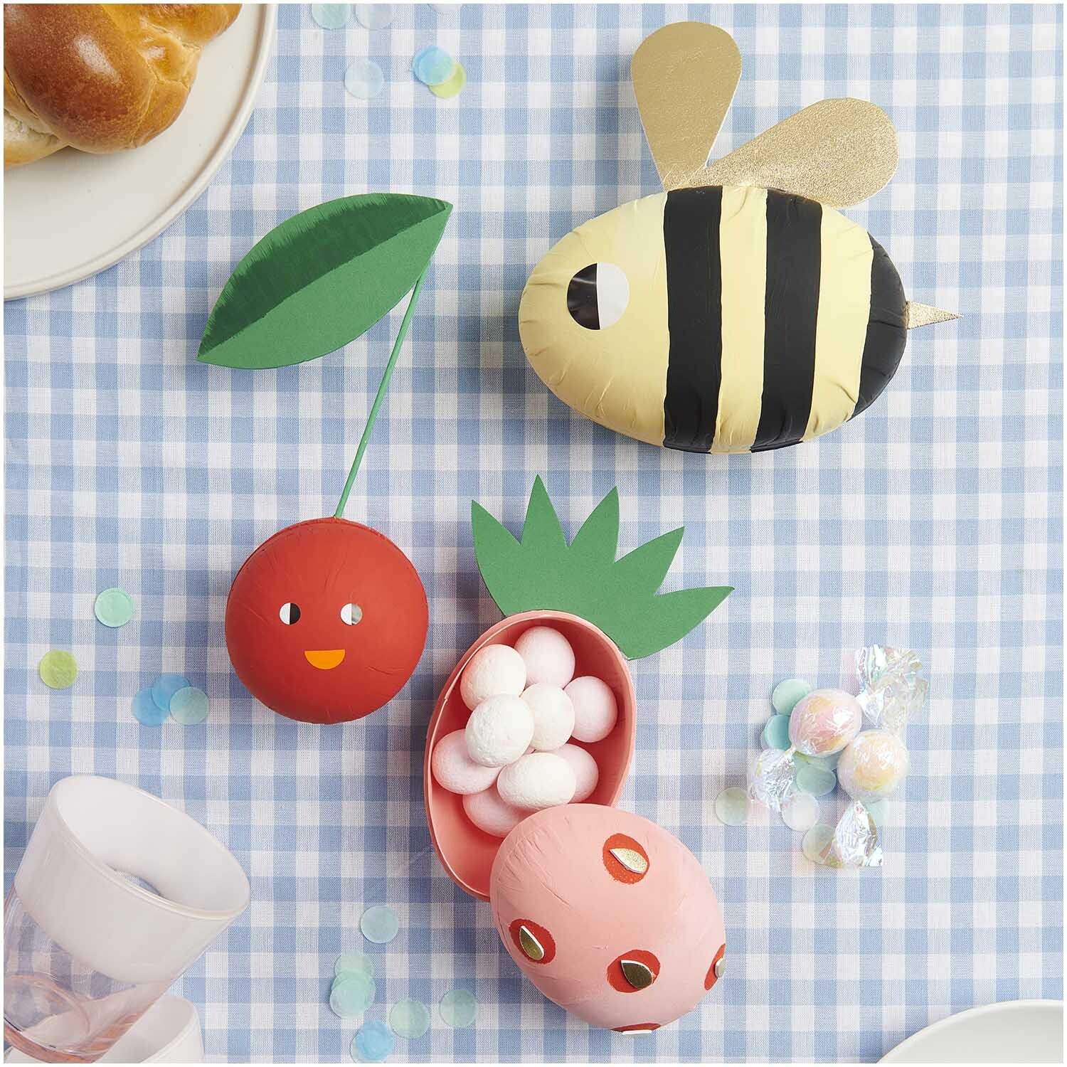 Pappmaché Kugel natur 8cm von Rico Design auf kariertem Tischtuch mit bunten Dekorationen.