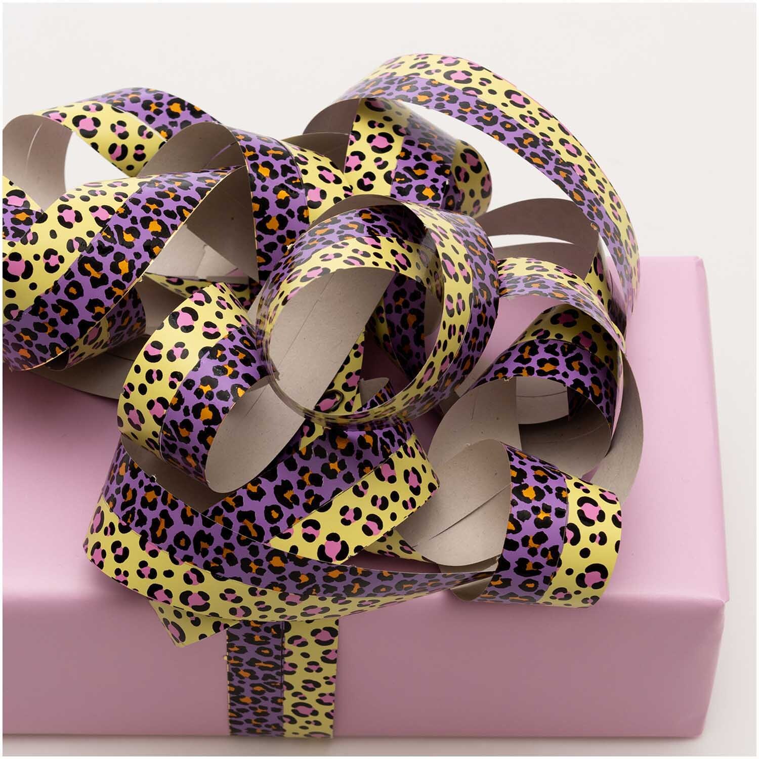 Luftschlangen Acid Leo gold 3,8m von Rico Design Luftschlangen Acid Leo gold 3,8m von Rico Design auf einem rosa Geschenk, mit Leopardenmuster in Lila und Gelb.