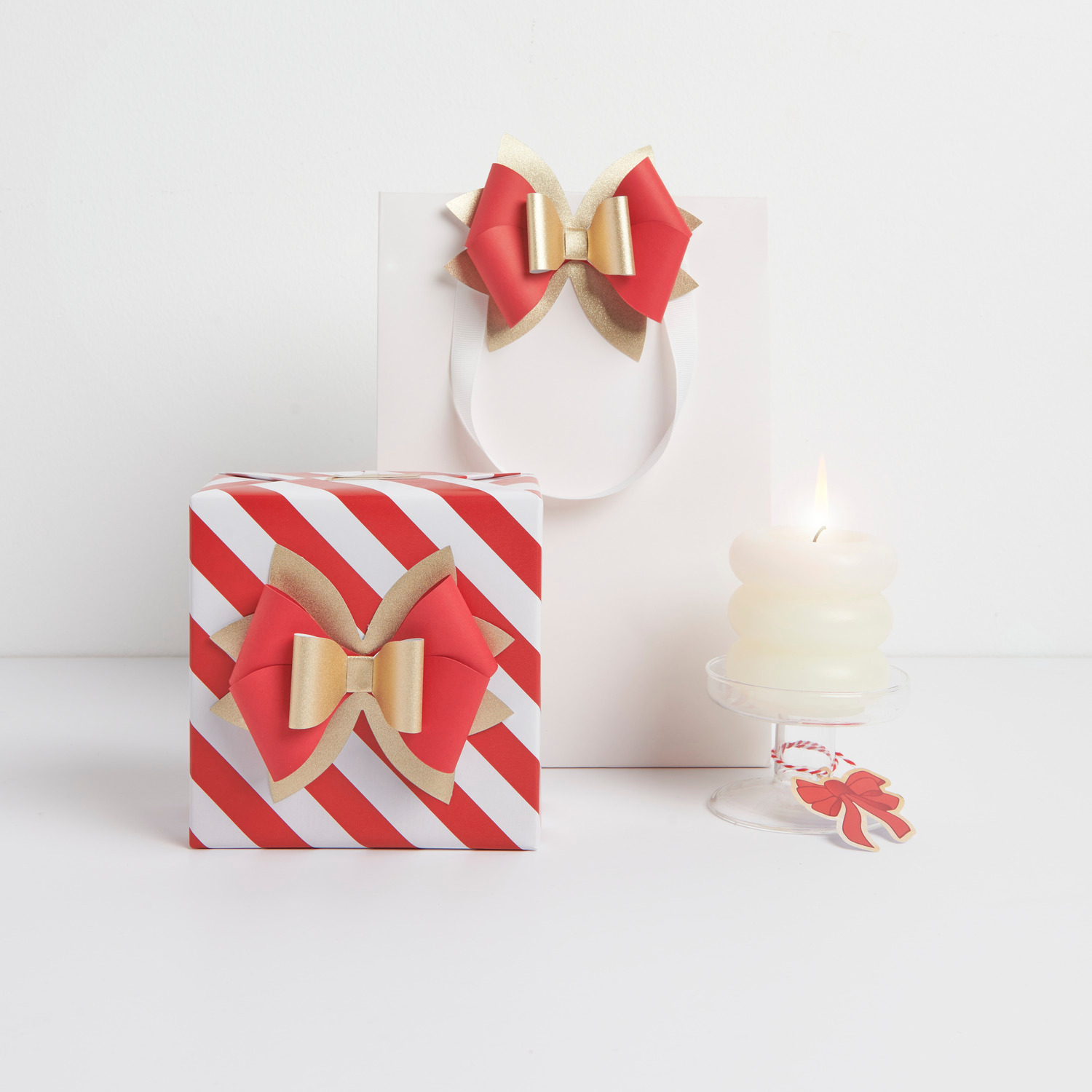 Papierschleife Rot/Gold 11,5x10cm 4 Stück von Rico Design Papierschleife Rot/Gold von Rico Design auf Geschenk und Tüte, dekoriert mit Kerze.