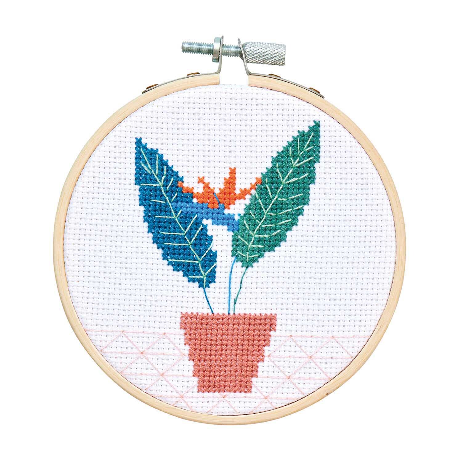 Stickpackung Mini Kit Strelitzie zeigt ein gesticktes Blumenmotiv in Blau und Orange in einem Holzrahmen. Ideal für DIY-Projekte.