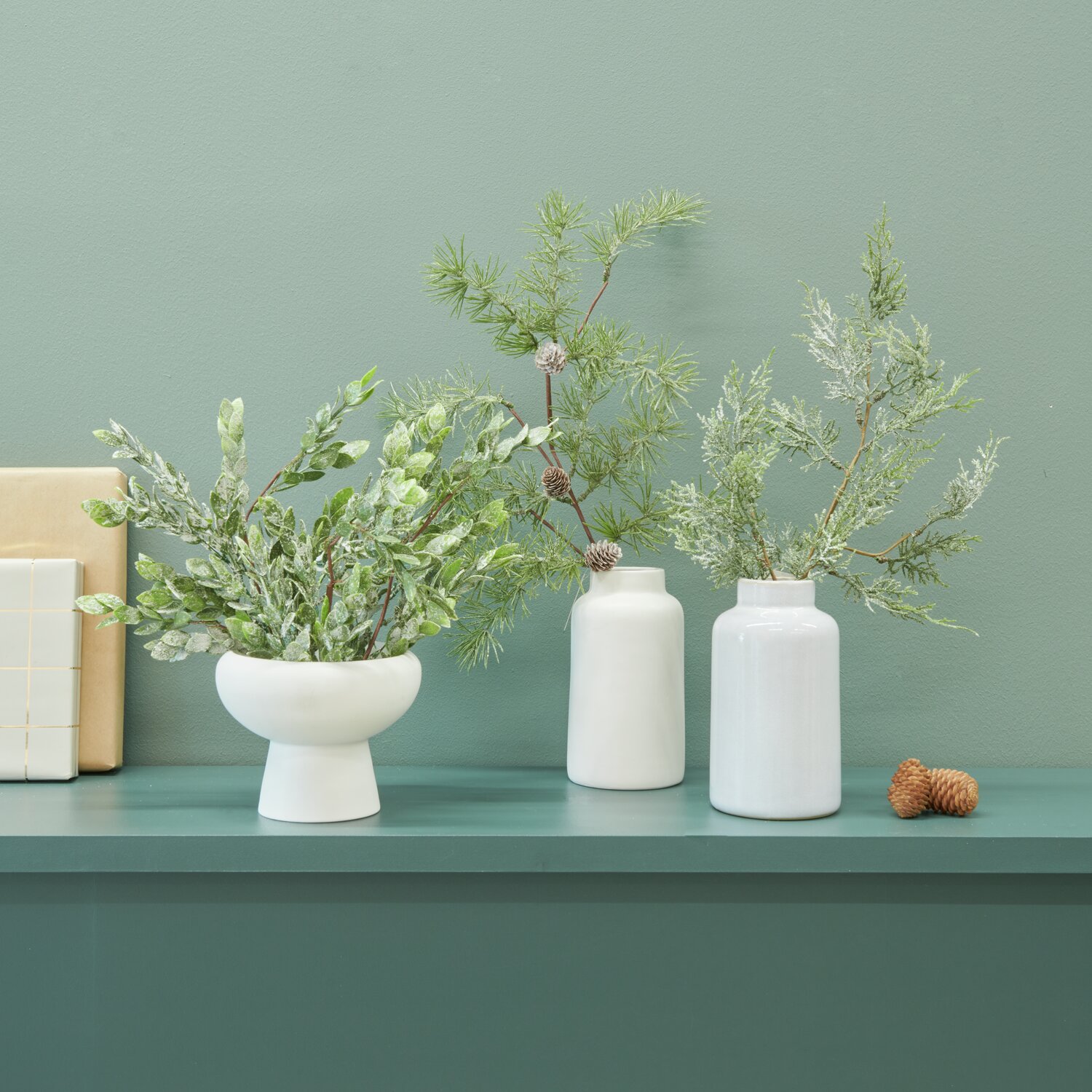 Porzellanvase mit geeistem Tannenzweig und Blätterzweig in weißer Schale, dekorativ arrangiert.