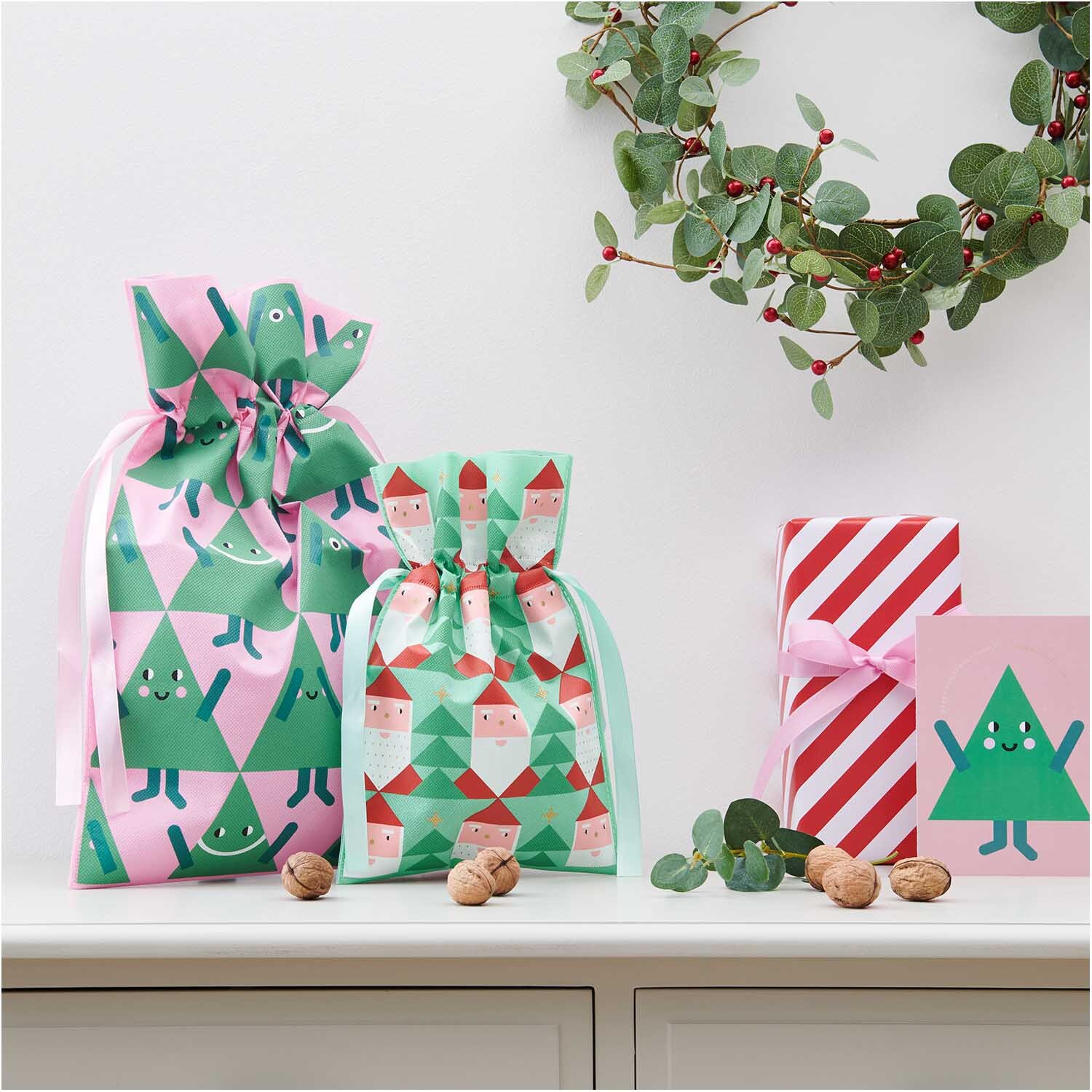 Geschenktüte Tannen groß 30x45cm von Rico Design Geschenktüte Tannen groß 30x45cm: Bunte Geschenktüten mit Tannenbaum-Motiven, umgeben von Nüssen und Dekoration.