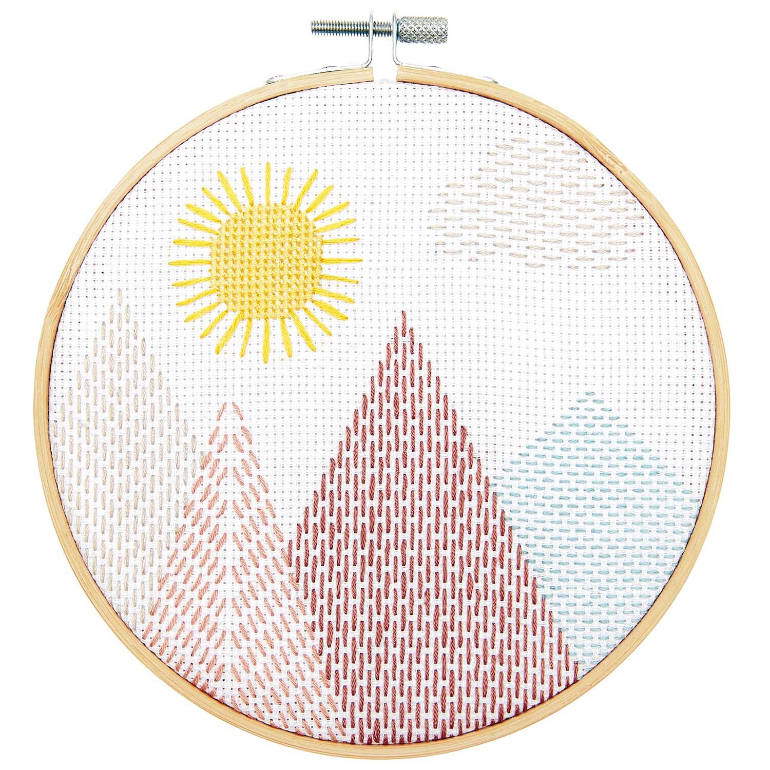 Stickpackung Sashiko Landschaft von Rico Design zeigt bunte Berge und eine gelbe Sonne im Stickrahmen.