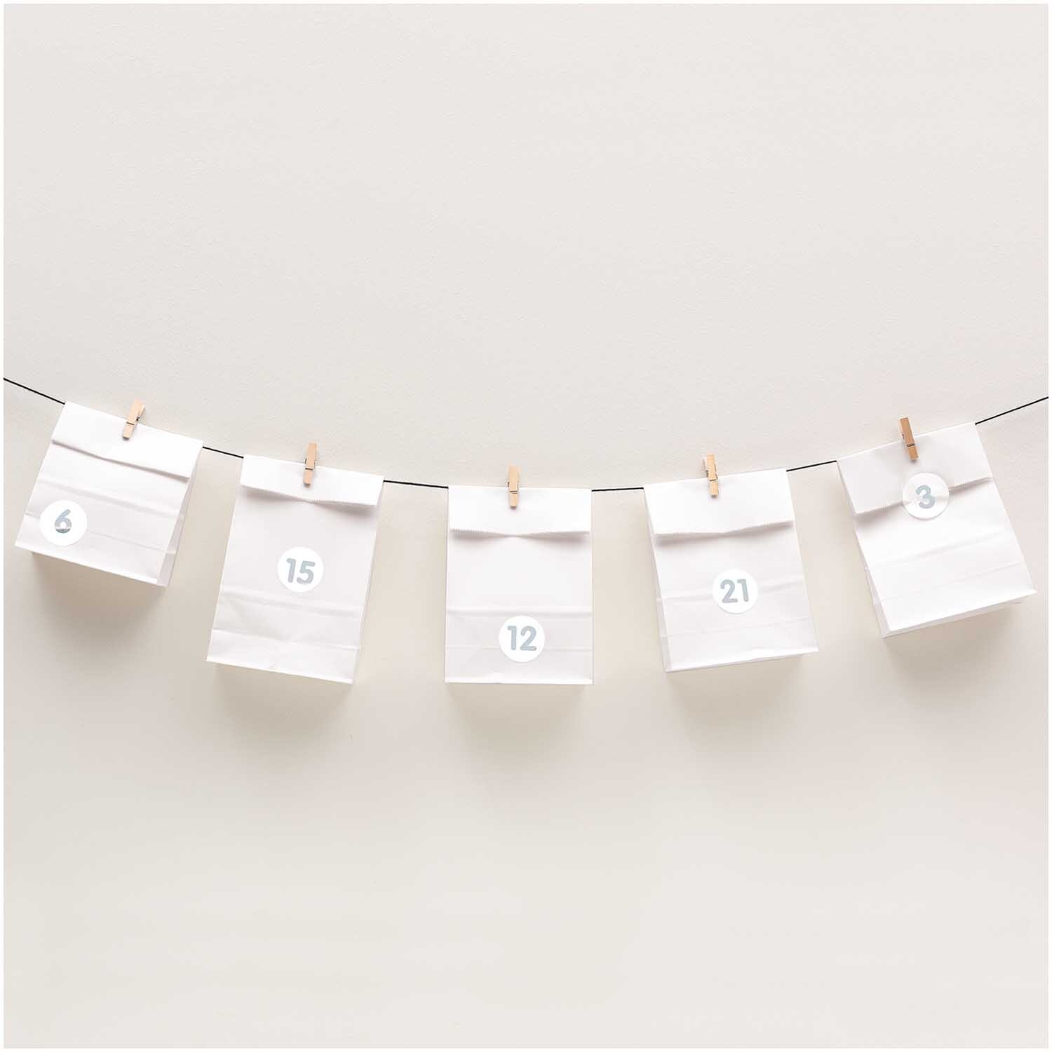 Paper Poetry Adventskalenderset: Fünf weiße Tüten mit Zahlen, aufgehängt an einer Schnur.