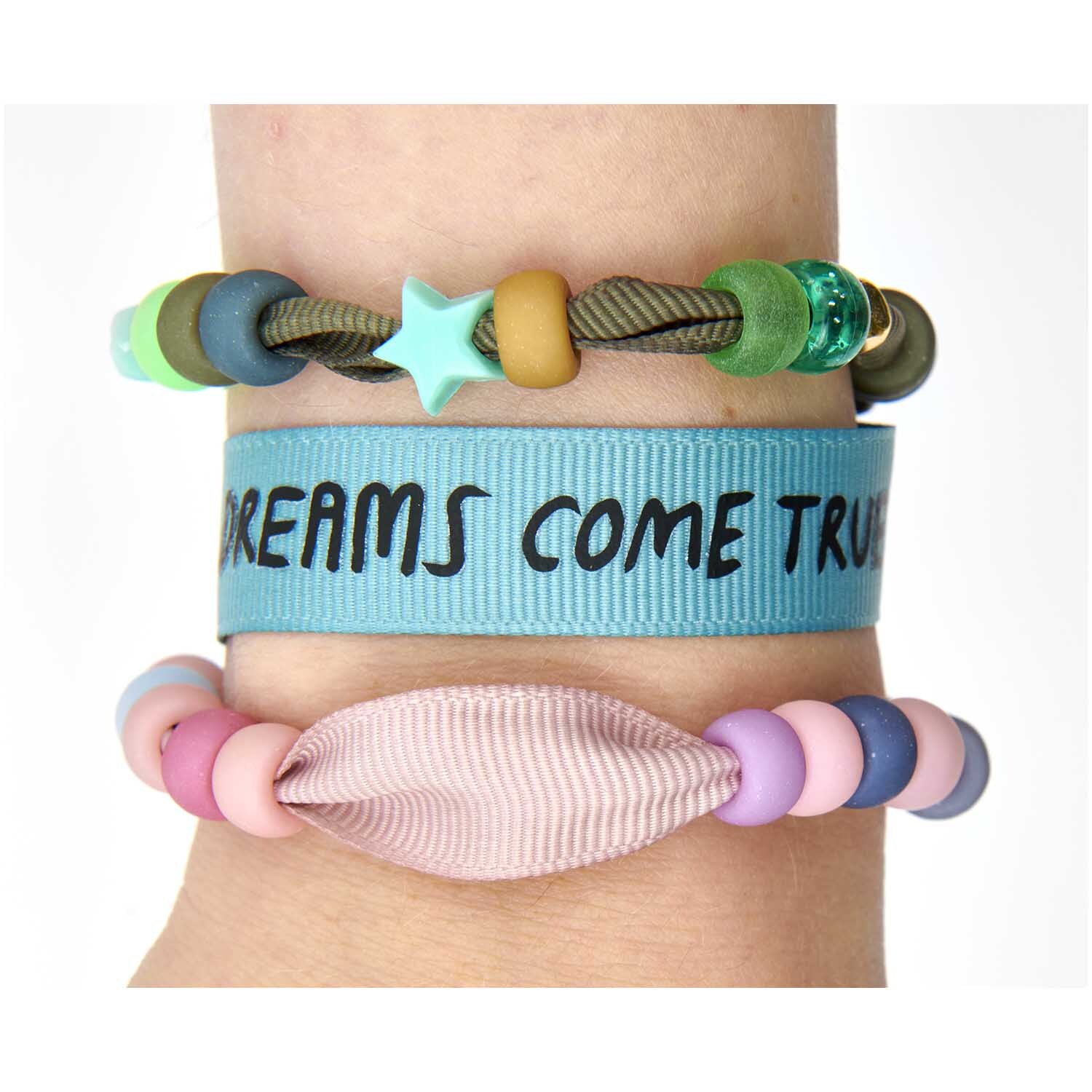 itoshii - Ponii Beads Ripsband Armbänder Erdfarben 10 Stück von Rico Design Itoshii - Ponii Beads Ripsband Armbänder, 10 Stück in Erdfarben, zeigen bunte Perlen und ein Band mit "Dreams Come True" auf einem Arm.