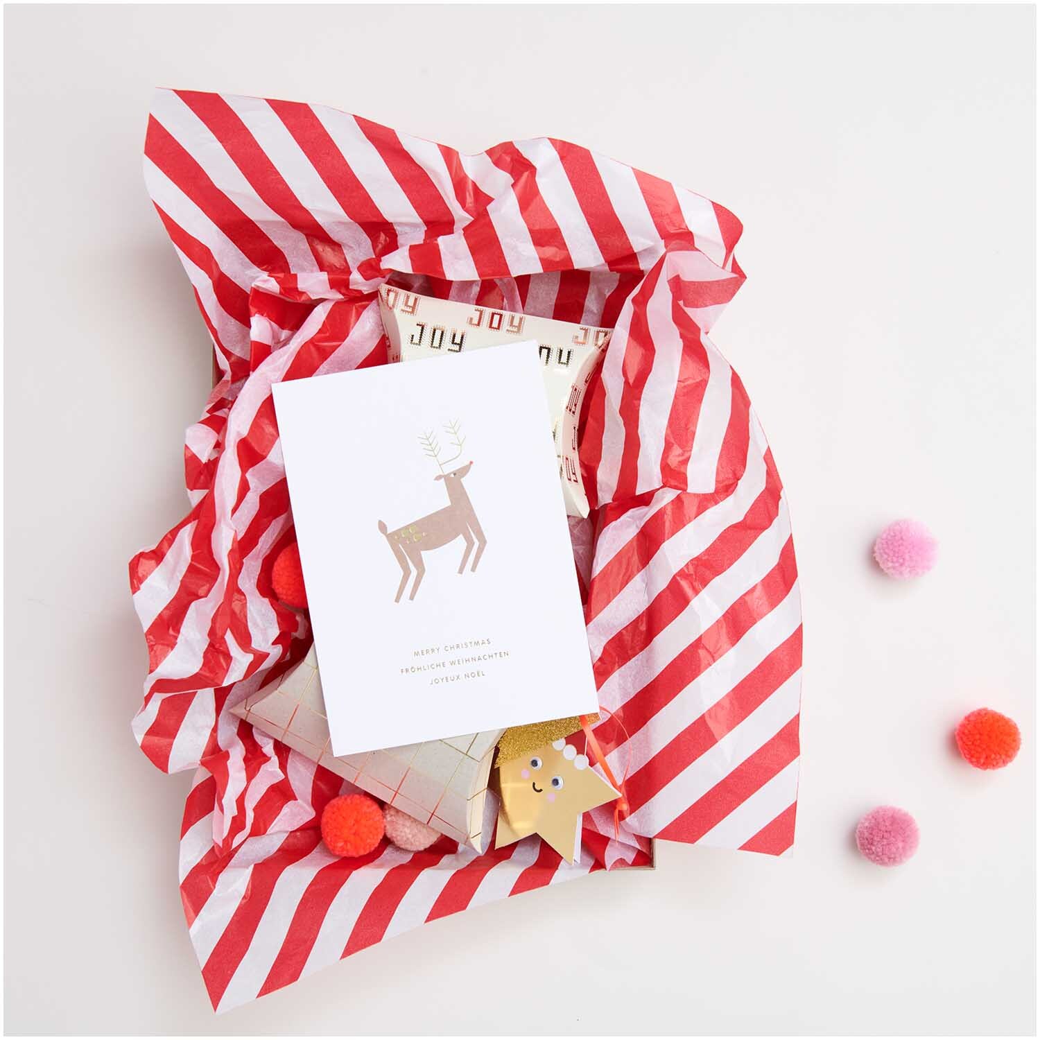 Paper Poetry Seidenpapier umhüllt Geschenke mit roten und weißen Streifen, dekoriert mit Pompons und einer Karte. Ideal für festliche Anlässe.