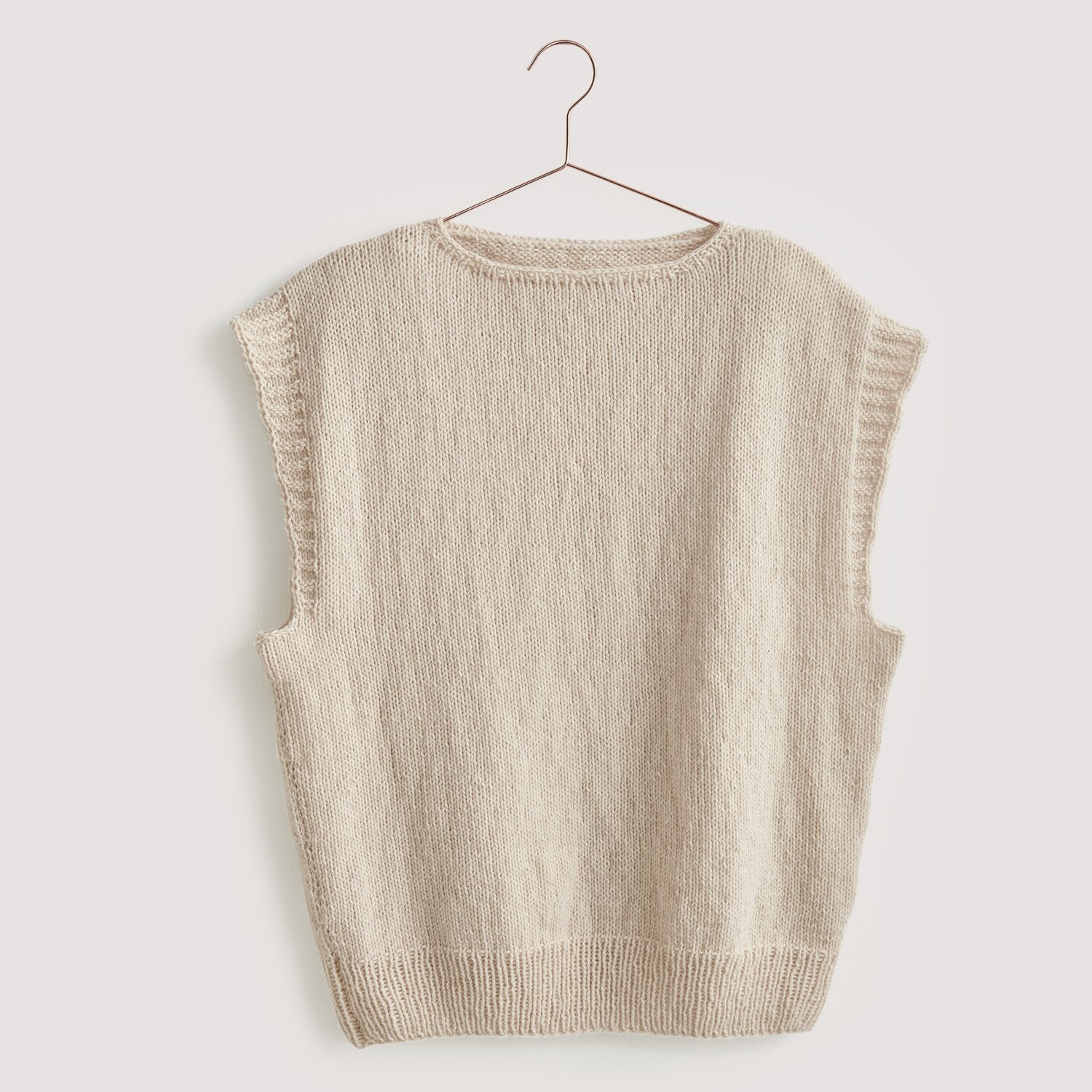 Luxury Merino Supercash dk 50g 160m Farbe Natur von Rico Design Strickset Pullunder Modell 03 aus Luxury Knits: Beiger Pullunder aus Premium Natural Fibres, hängend an einem Kleiderbügel.