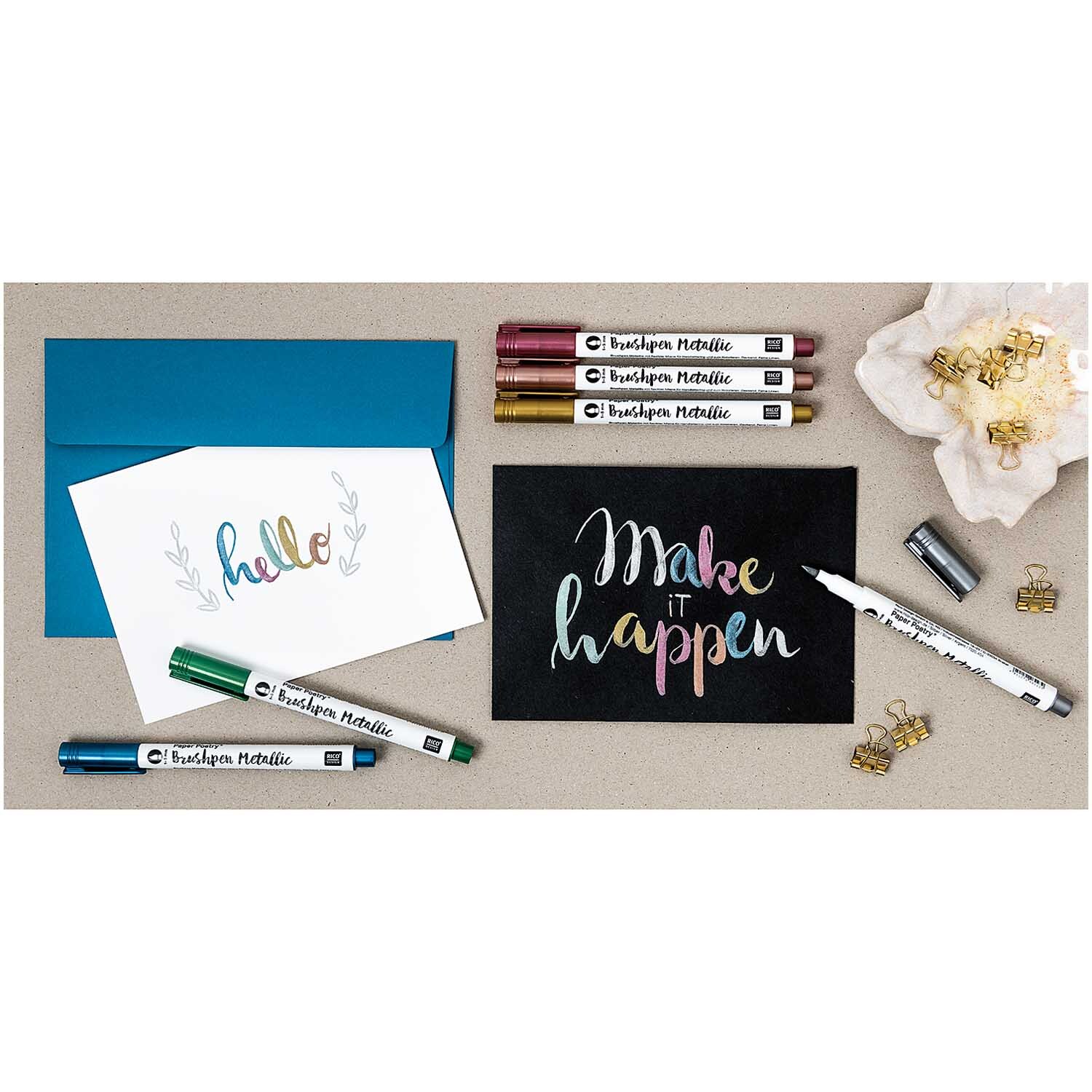 Paper Poetry Metallic Brushpen 1-5mm von Rico Design auf Karten mit Schriftzügen in verschiedenen Farben, umgeben von Briefumschlägen und Clips.