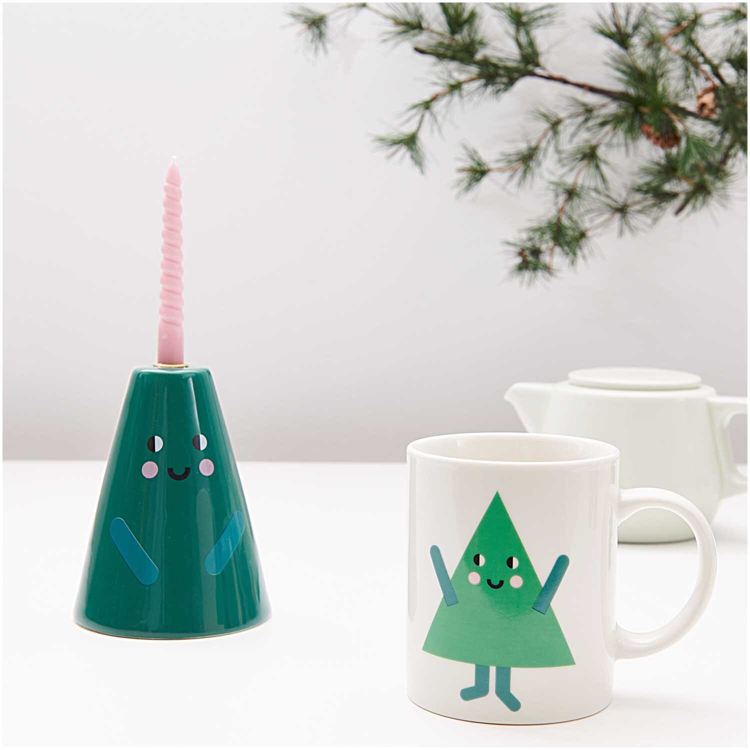 Porzellan Tasse Tanne 8x9,5cm von Rico Design Porzellan Tasse Tanne 8x9,5cm mit fröhlichem Tannenbaum-Design, neben einem grünen Kerzenhalter.