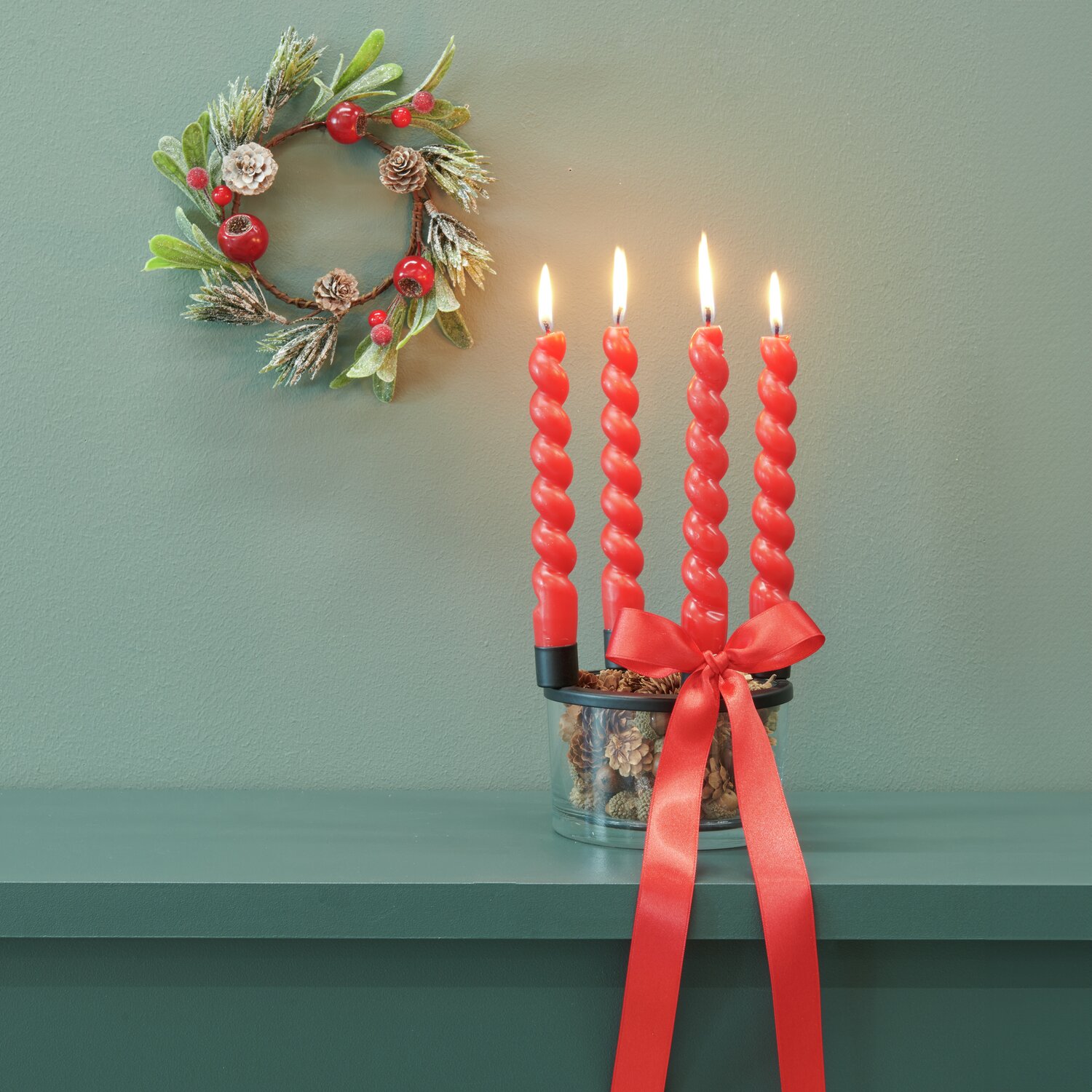 Advent-Metallkerzenhalter mit Glasvase, dekoriert mit roten Spiralkerzen und Tannenkranz.