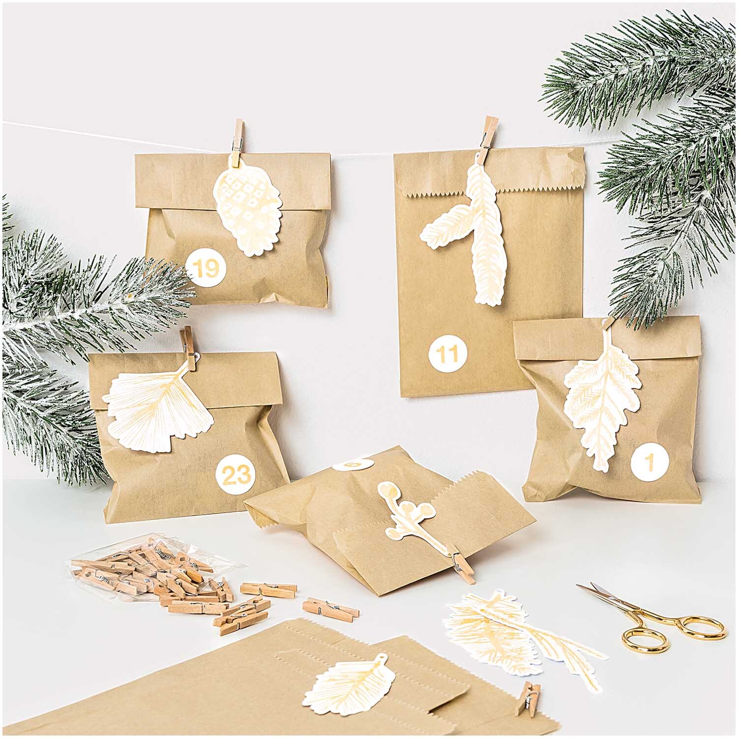 Paper Poetry Papieranhänger Nostalgic Christmas: Goldene Zweige schmücken braune Geschenktüten, umgeben von Tannenzweigen und Holzklammern.