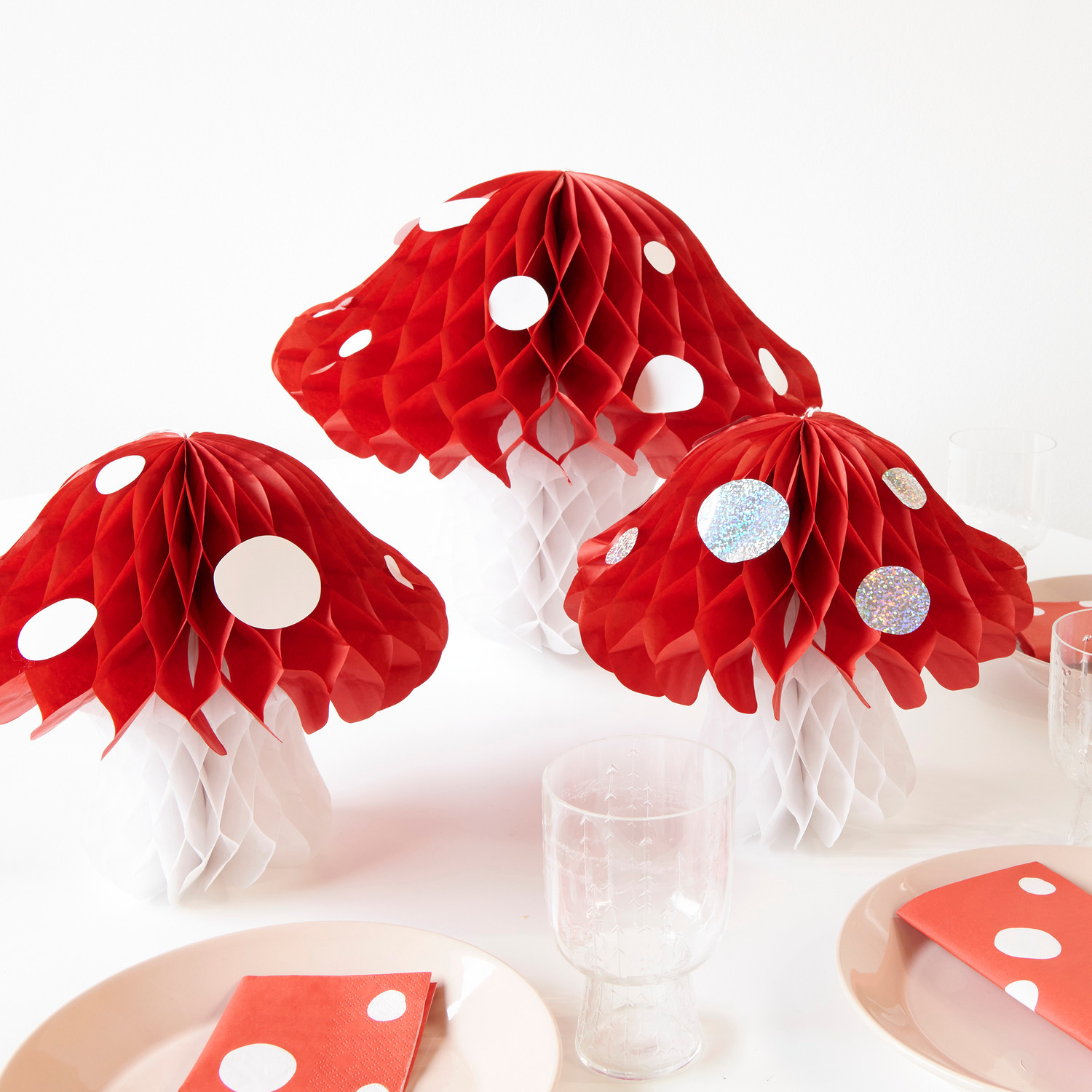 Servietten Fliegenpilz Muster 33x33cm 20 Stück von Rico Design Servietten Fliegenpilz Muster: Rote Wabenpapier-Dekorationen in Pilzform auf einem gedeckten Tisch.