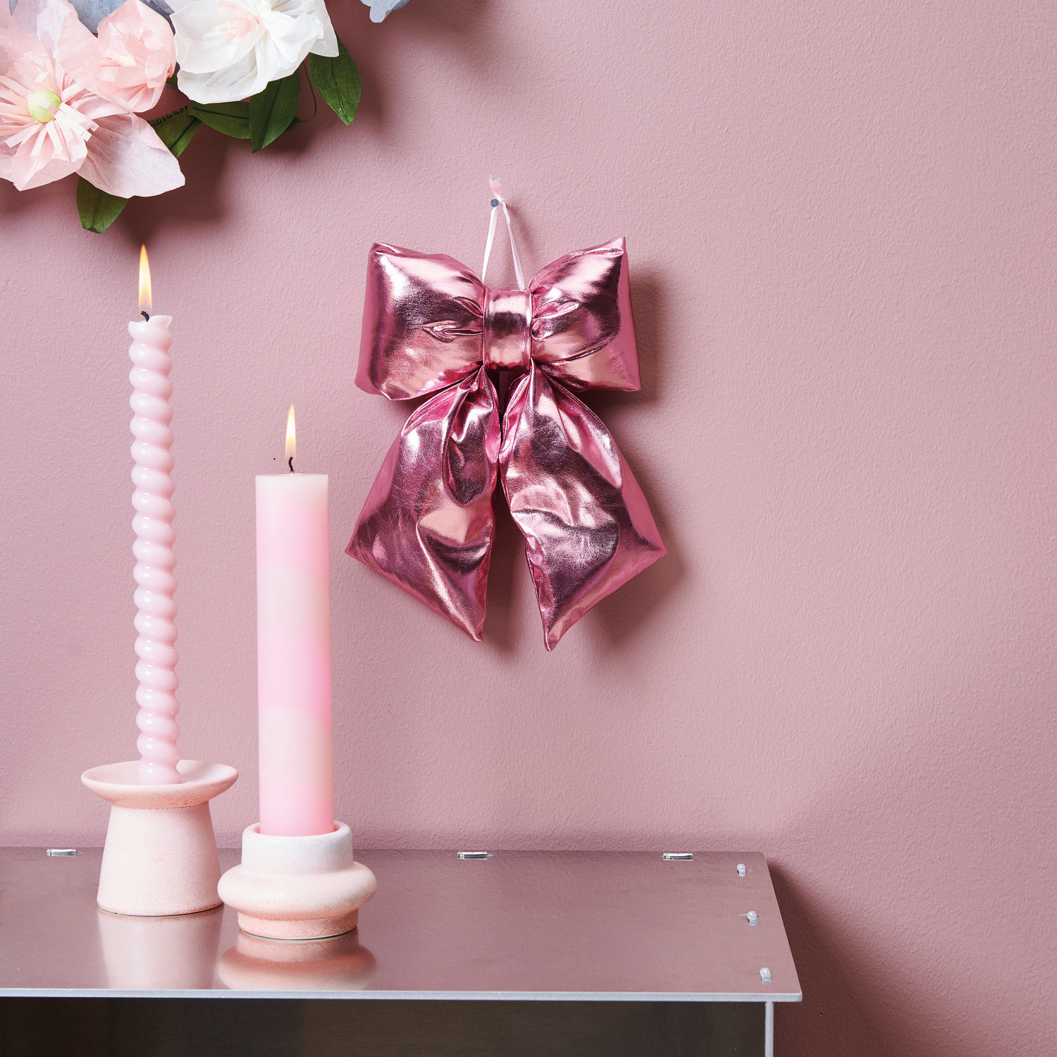 Blütenkranz Papier Rosé: Dekorative Schleife in Pink mit Kerzenhalter und Spiralkerze auf rosa Hintergrund.