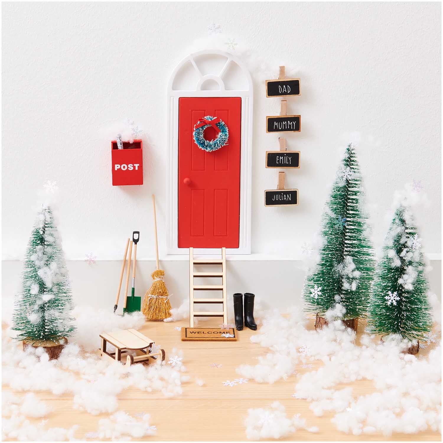 Miniatur Wichteltür mit Bogen, umgeben von Dekorationen wie Bäumen, Schlitten und Schneeflocken.