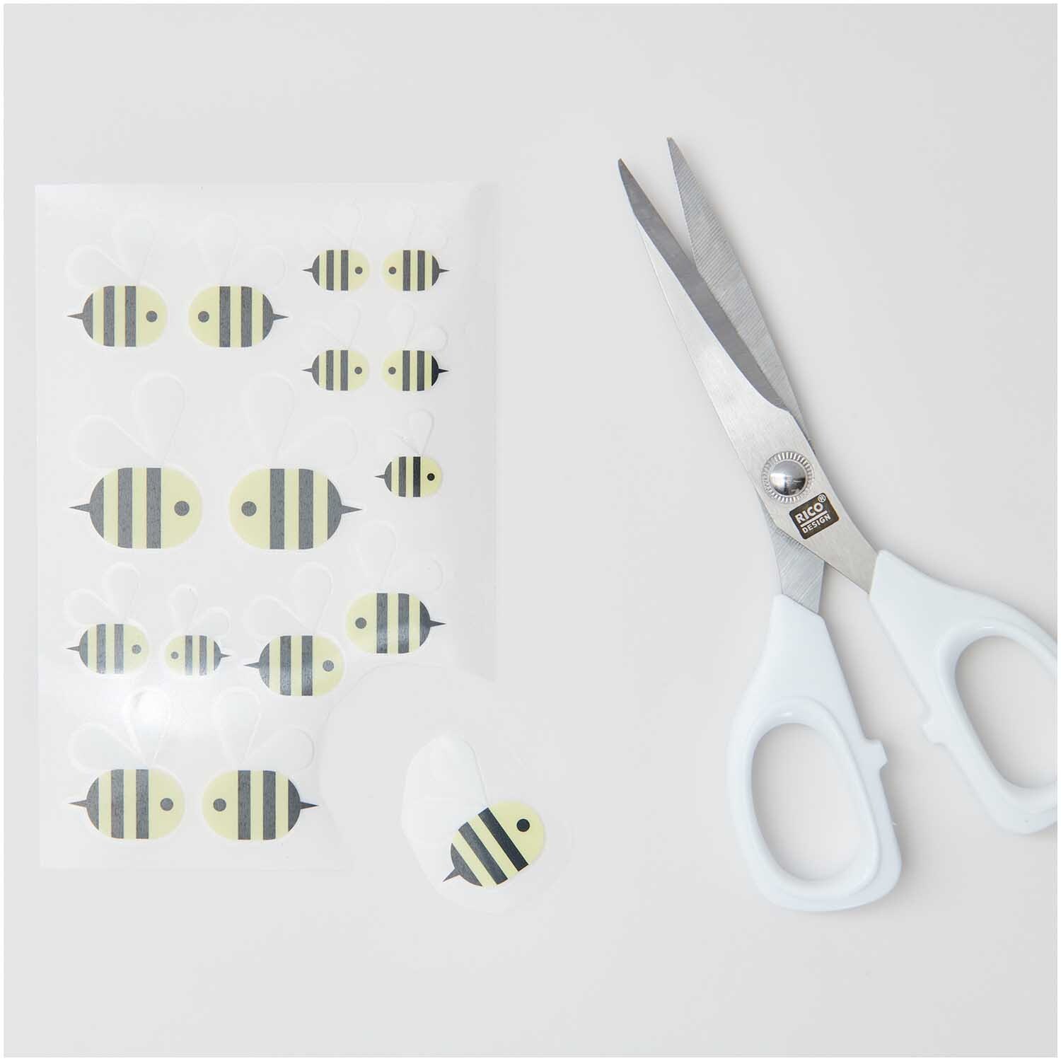 Transfermotiv Biene 15 Stück von Rico Design Transfermotiv Biene: 15 gelb-schwarze Bienenmotive von Rico Design neben einer weißen Schere auf grauem Hintergrund.