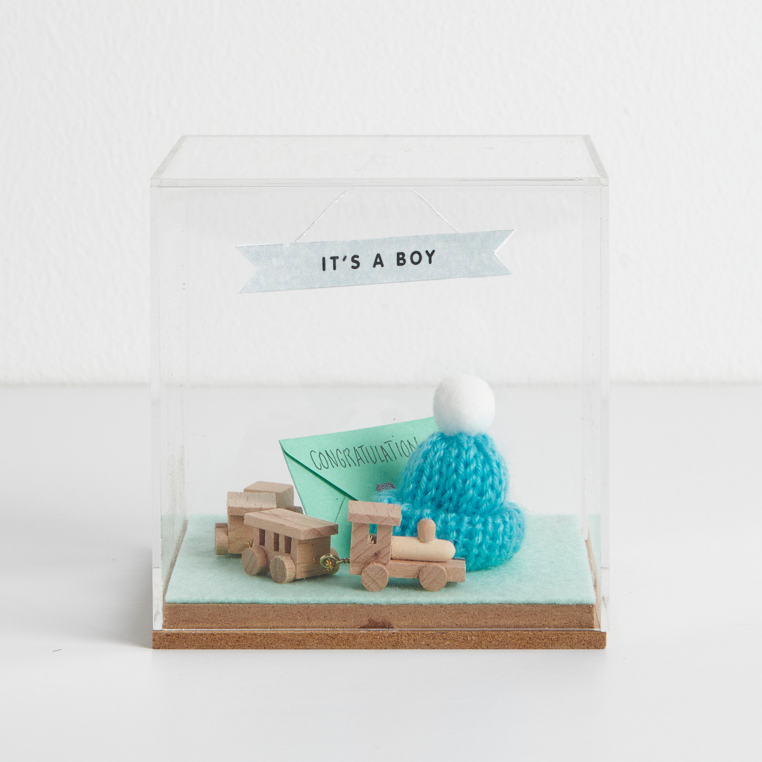 Figurico Dekohaube Würfel Größe 6x6x6,5cm von Rico Design Figurico Dekohaube Würfel mit Holzspielzeugzug, blauem Strickmütze und "It's a Boy"-Banner. Ideal als Geschenk zur Geburt.