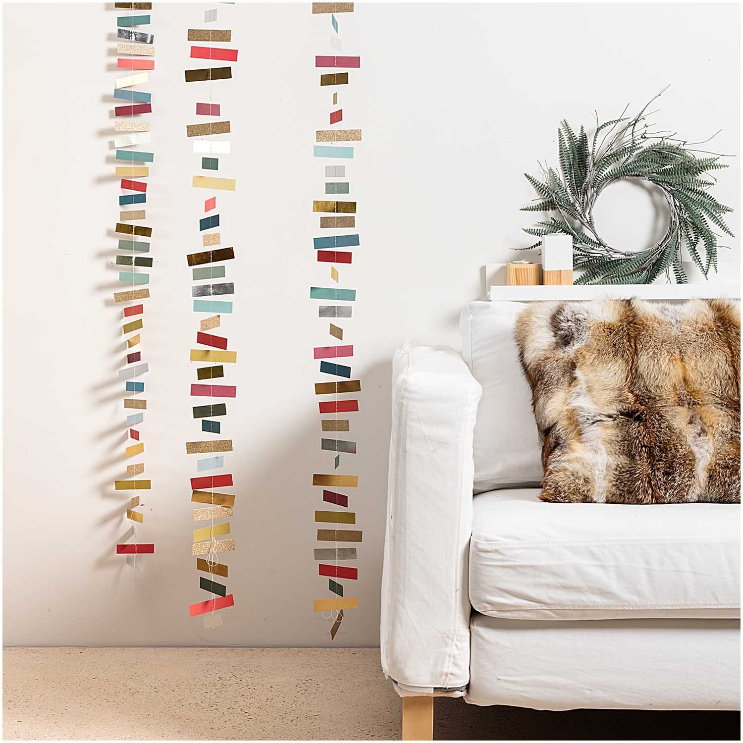 Genähte Girlande Streifen classic 1,8m von Rico Design Genähte Girlande Streifen classic 1,8m von Rico Design in bunten Farben, dekorativ an einer weißen Wand neben einem Sofa.