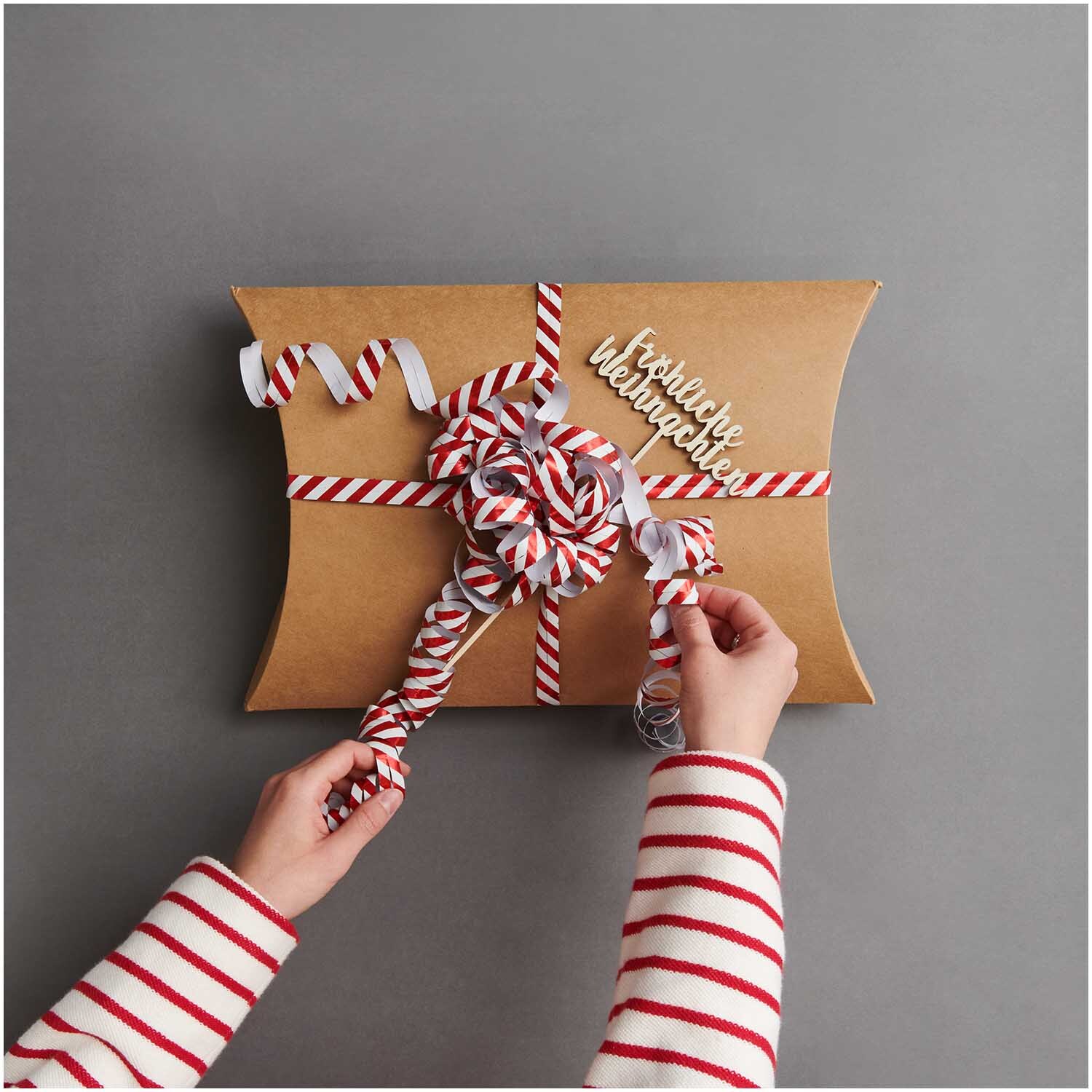 Luftschlangen Streifen rot-weiß 3,8m von Rico Design Luftschlangen Streifen rot-weiß 3,8m: Geschenkverpackung mit rot-weißen Streifen und Schleife. Hände binden dekorative Schleife.