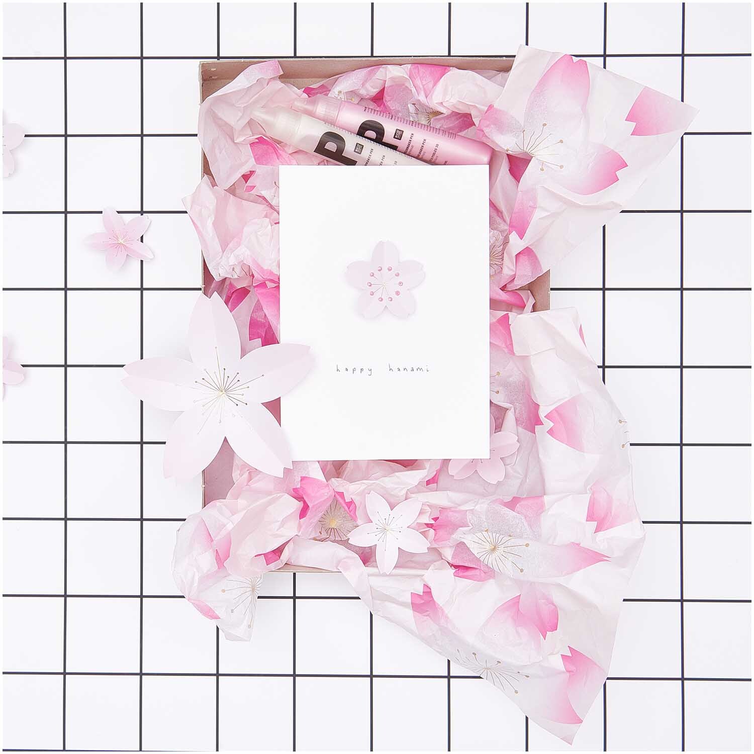 Paper Poetry Seidenpapier zeigt Kirschblütenmuster in Rosa, dekoriert mit Blumen auf kariertem Hintergrund. Ideal für kreative Projekte.