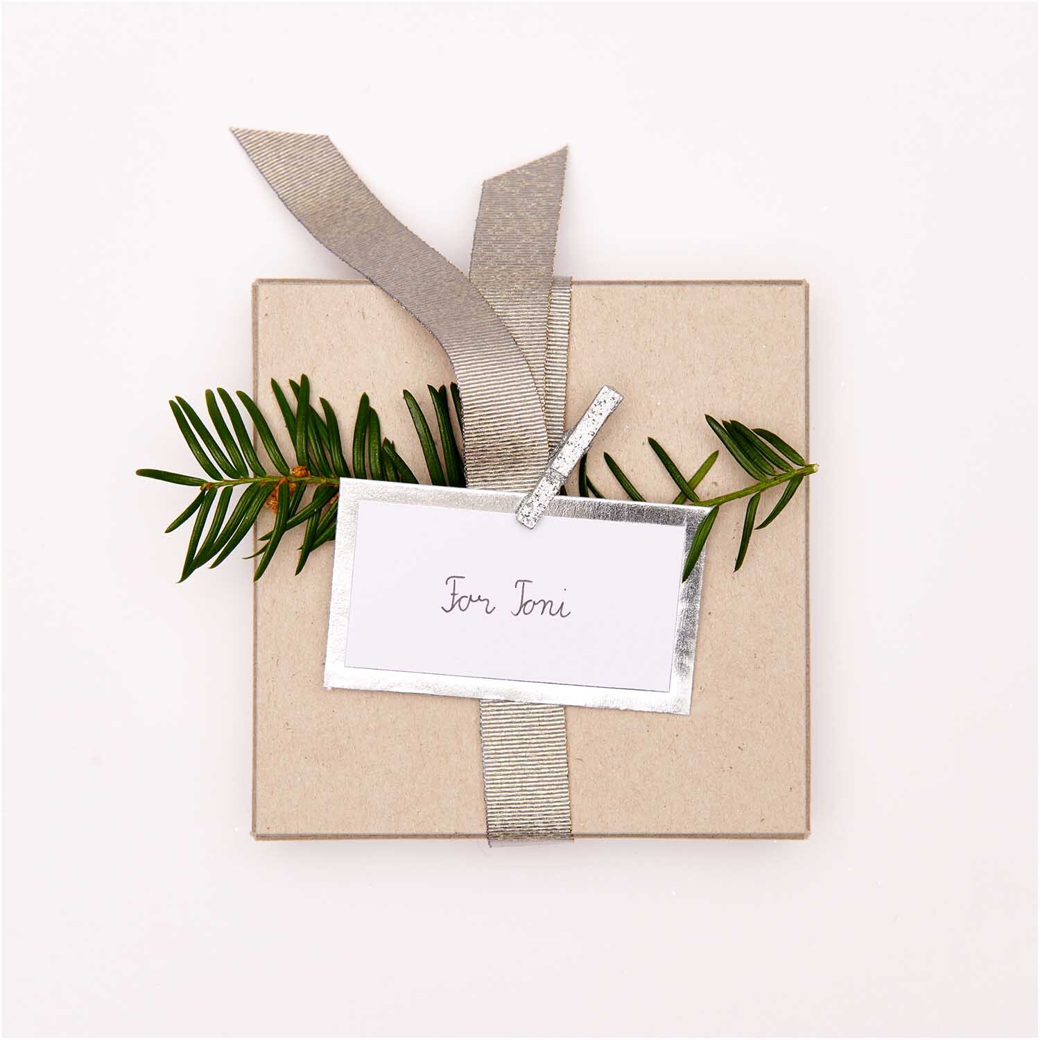Paper Poetry Papierkärtchen mit Hot Foil auf Geschenk mit Zweig und silbernem Band dekoriert.