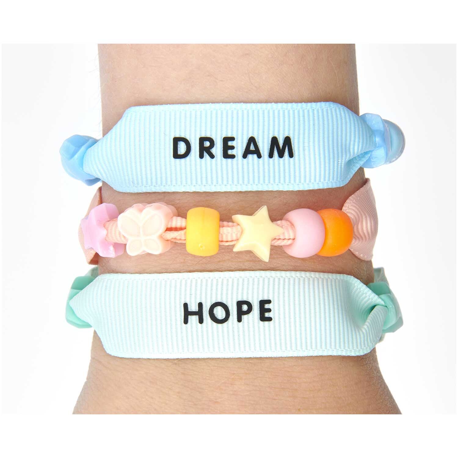 itoshii - Ponii Beads Ripsband Armbänder pastell 10 Stück von Rico Design Itoshii - Ponii Beads Ripsband Armbänder in Pastellfarben mit Botschaften "Dream" und "Hope", dekoriert mit bunten Perlen.