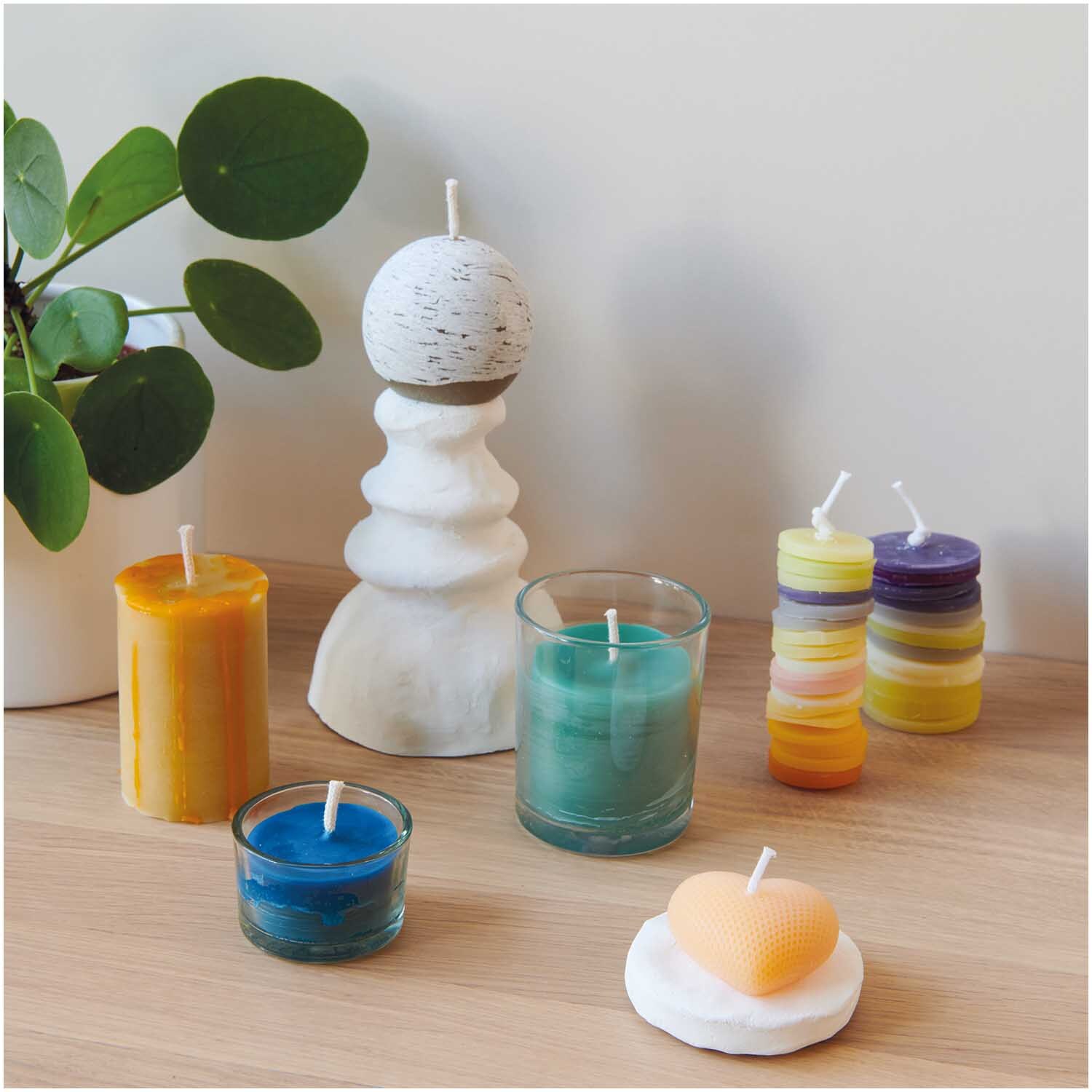 Kerzenglas Größe 8x9cm von Rico Design Kerzenglas auf Holzoberfläche mit bunten Kerzen und Pflanzen im Hintergrund für gemütliche Atmosphäre.