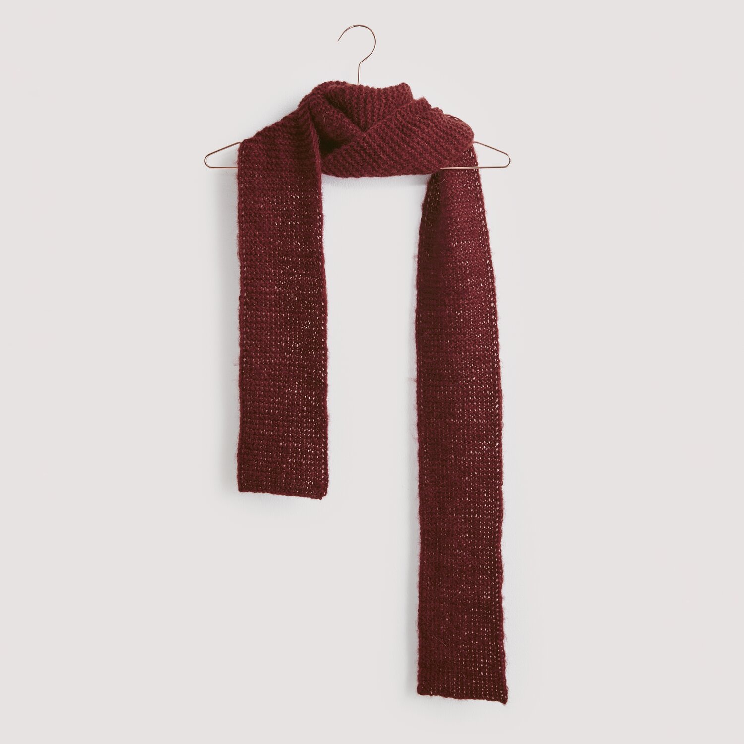Luxury Merino Alpaca Dream aran 50g 125m Farbe Bordeaux von Rico Design Strickset Schal Modell 17 aus Luxury Knits, dunkelroter Schal aus Premium Natural Fibres, hängt an einem Kleiderbügel vor grauem Hintergrund.